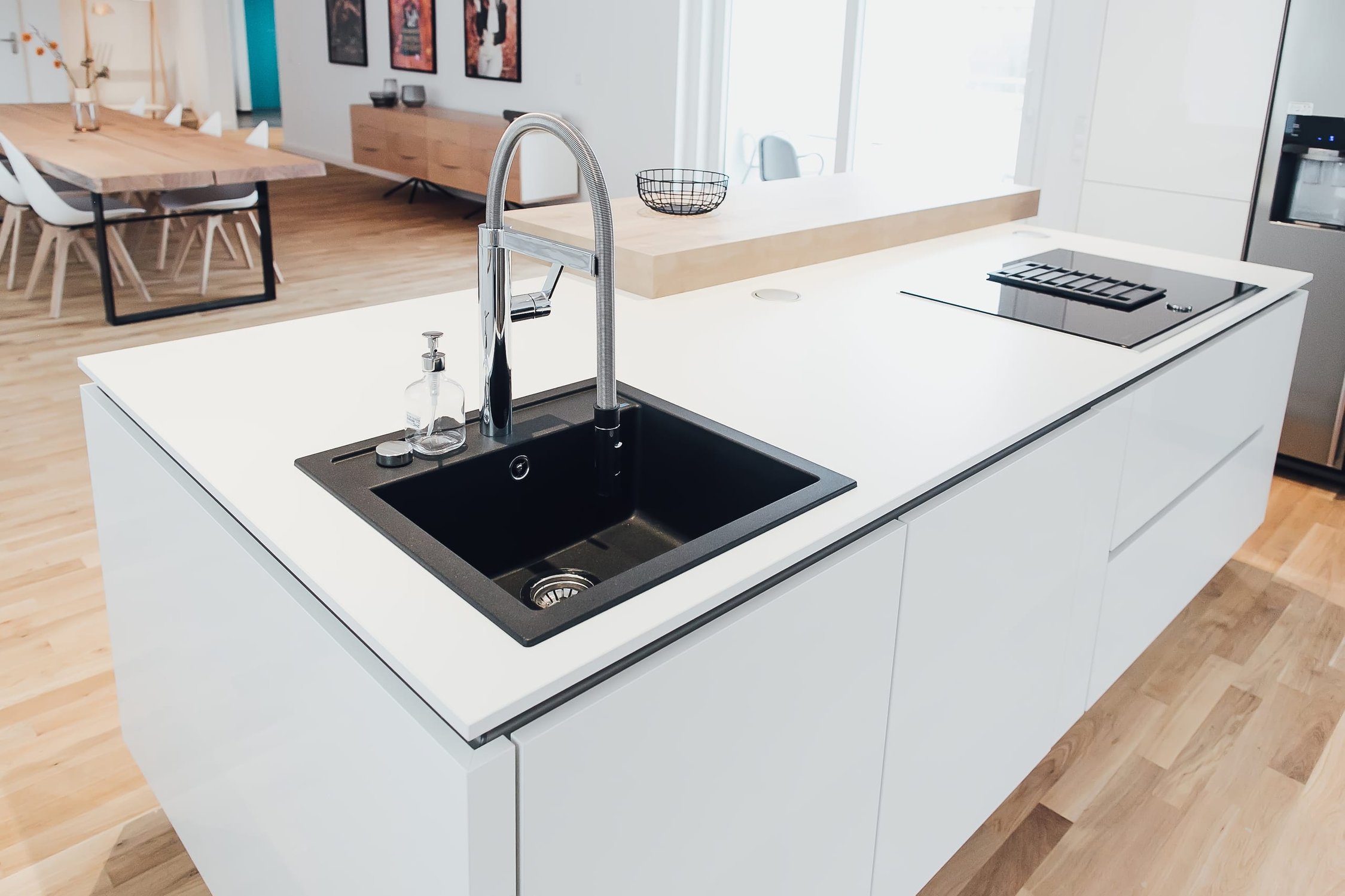 Moderne helle Küche mit Kücheninsel, schwarzer Spüle und Induktionskochfeld, Holzfußboden