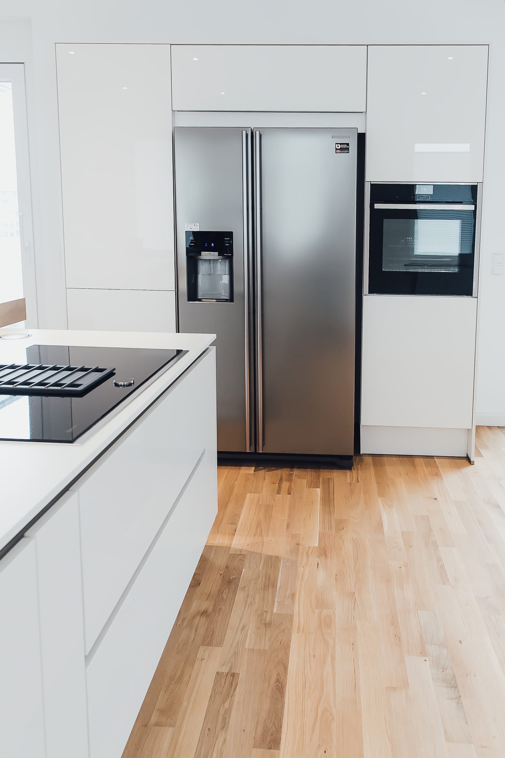 Moderne Küche mit weißen Schränken, Edelstahlofen und -kühlschrank, heller Holzboden