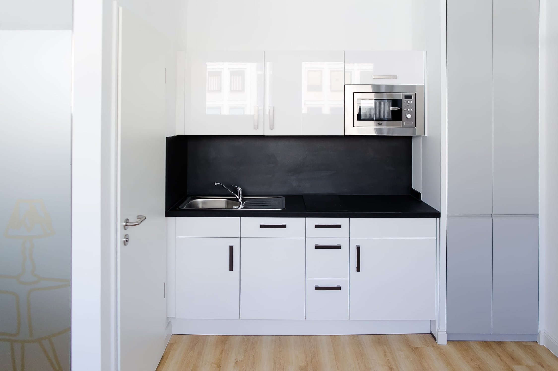 Moderne Küchenzeile mit weißen Hochglanzfronten, schwarzer Arbeitsplatte, Spüle und Mikrowelle