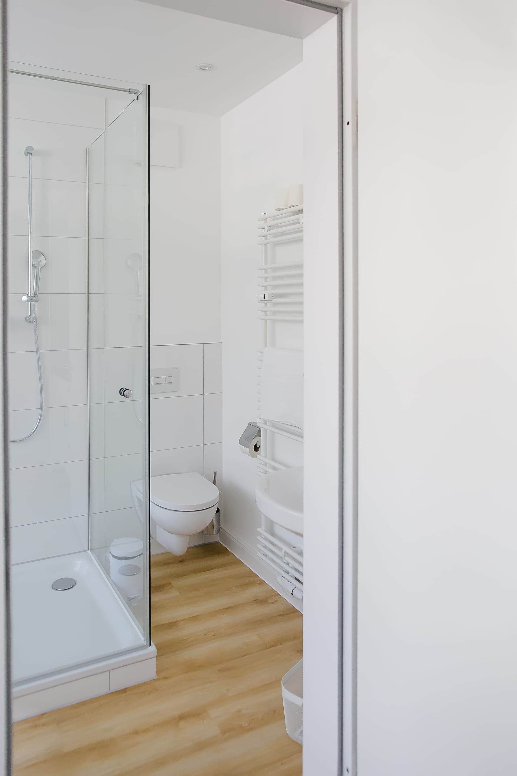 Helles Bad mit Holzfußboden, rahmenloser Duschkabine, WC, weißem Handtuchtrockner