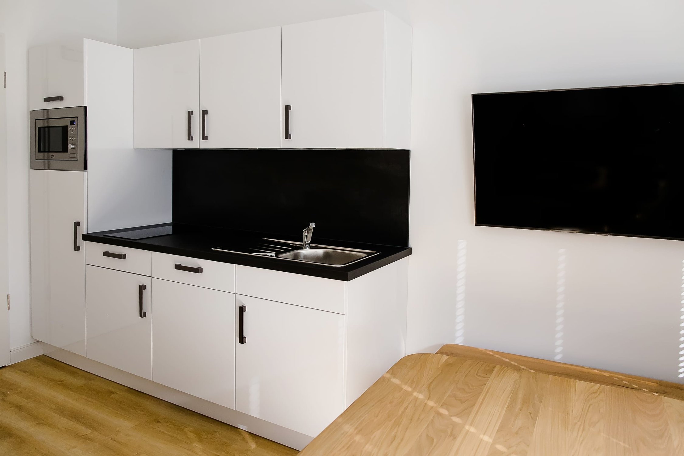 Kleine Küchenzeile mit weißen Schränken, schwarzen Arbeitsplatten, Spüle und Mikrowelle