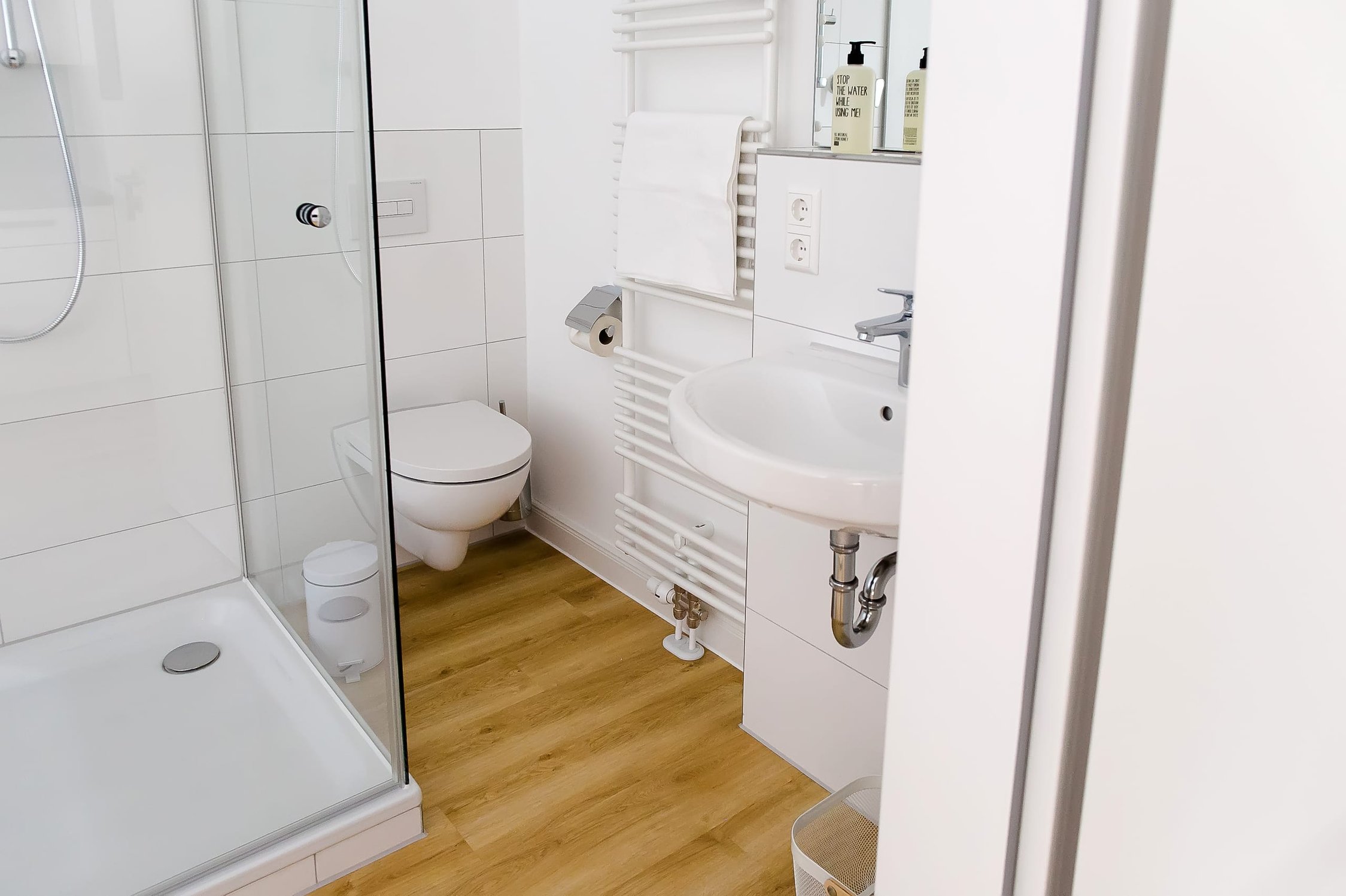 Modernes Badezimmer mit Holzboden, weißer Dusche, Toilette und Waschbecken