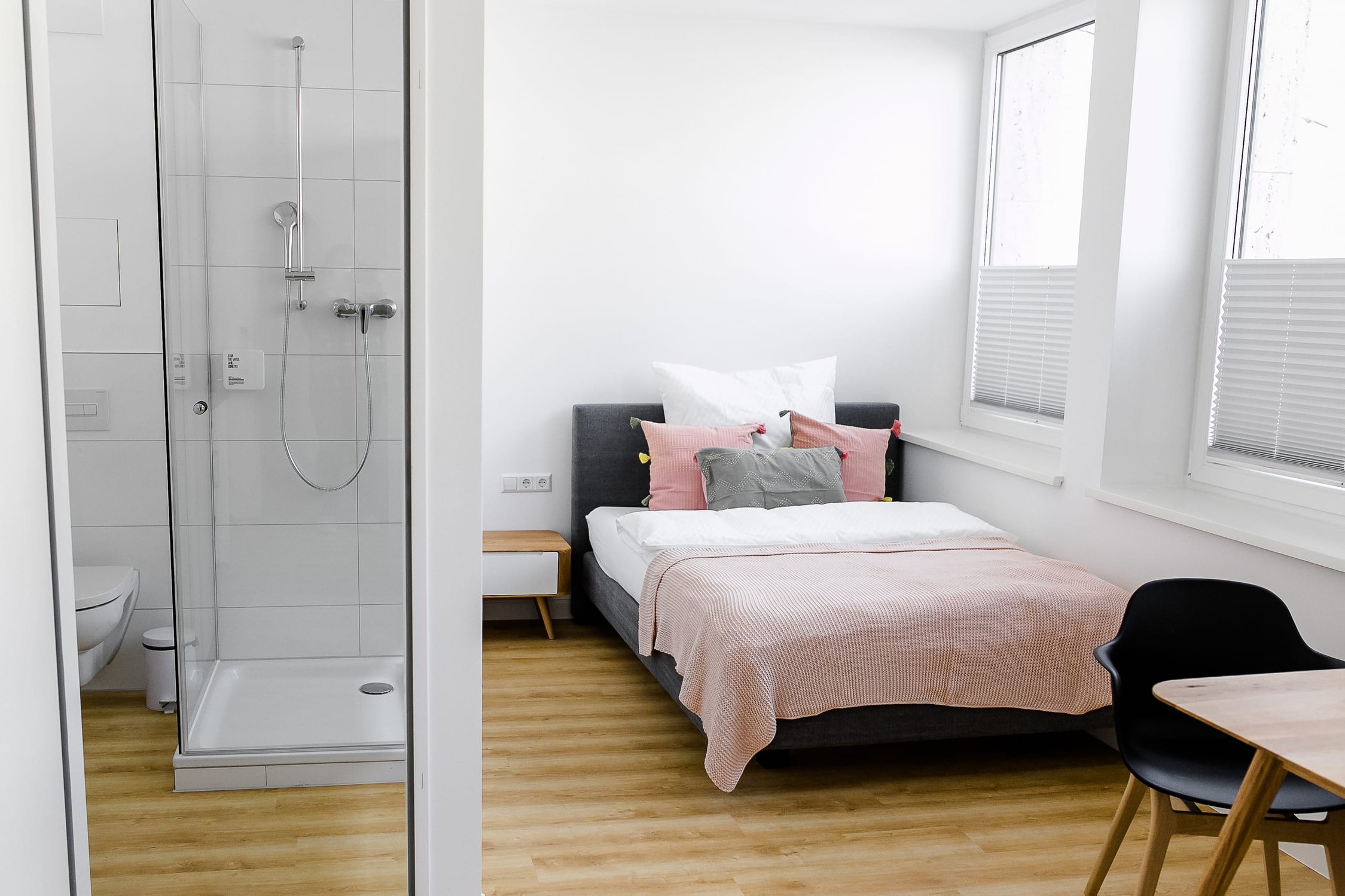 Schlafzimmer mit grauem Bett, rosa Überwurf und einem Badezimmer mit Duschkabine