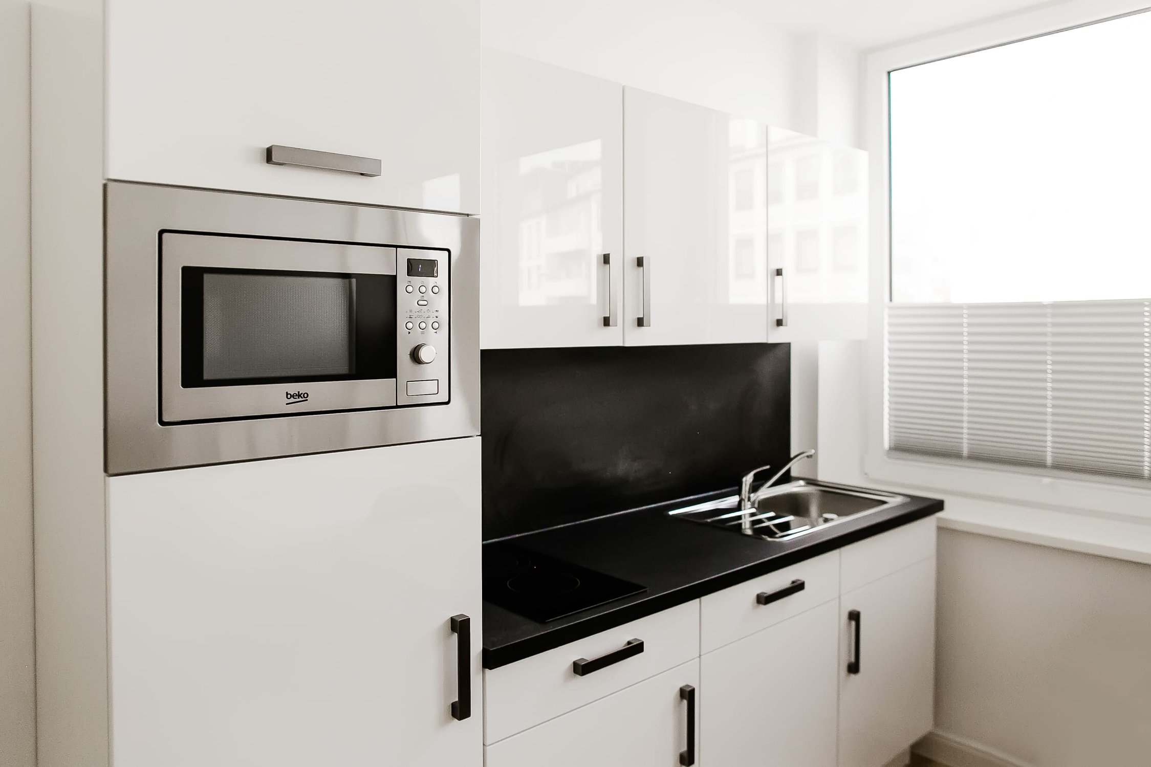 Moderne Küche mit weiß glänzenden Schränken, Edelstahl-Mikrowelle und schwarzer Arbeitsplatte
