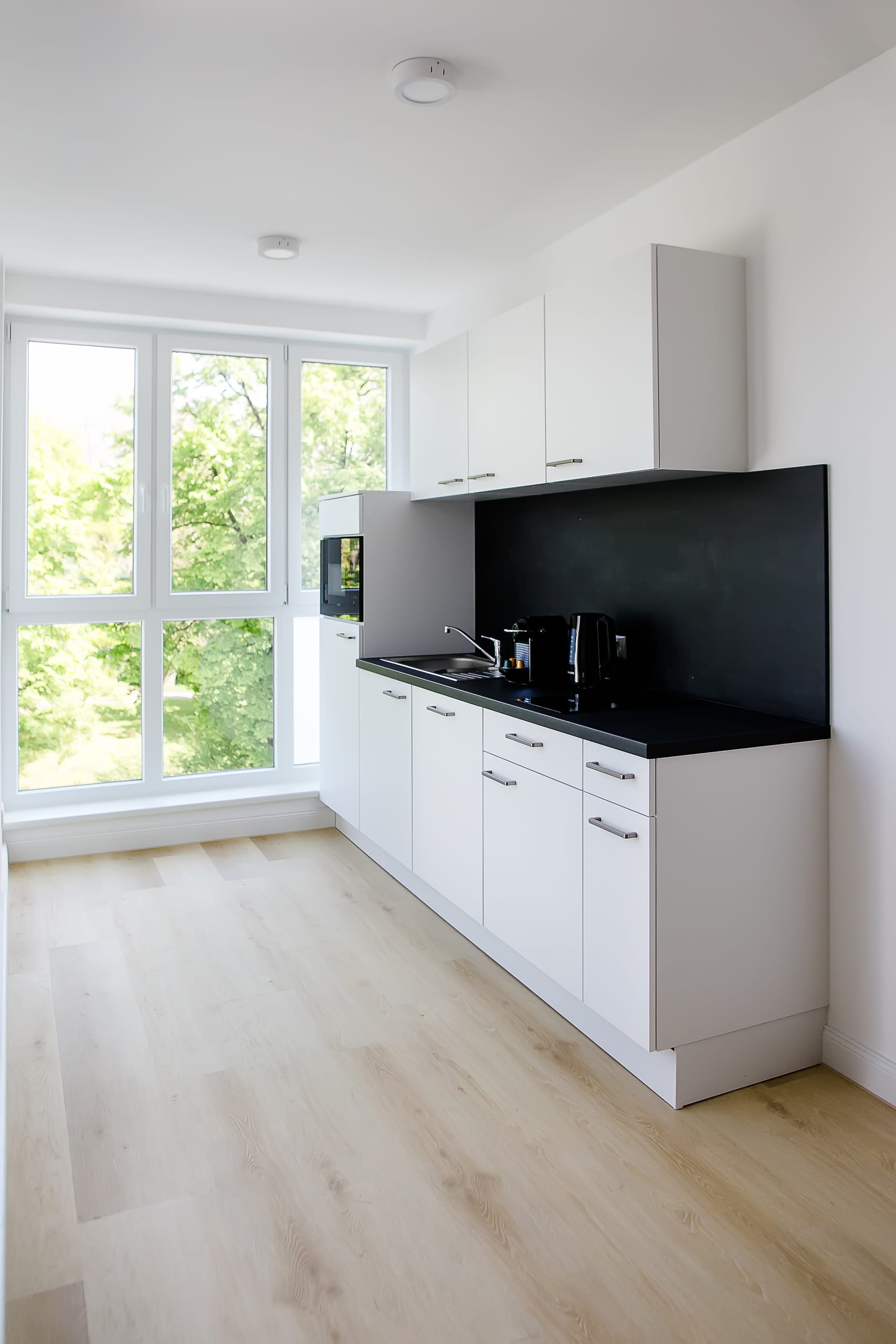 Helle Küche mit weißen Schränken, dunkler Arbeitsplatte, Holzboden und großem Fenster