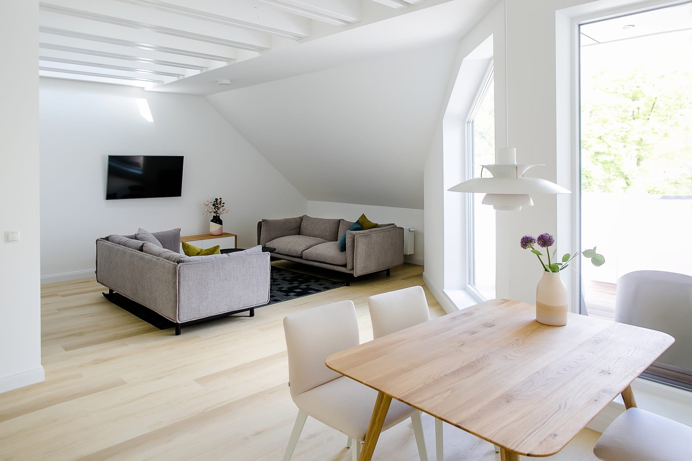 Helles Wohnzimmer mit zwei grauen Sofas und Esstisch, großflächigen Fenstern, Holzboden