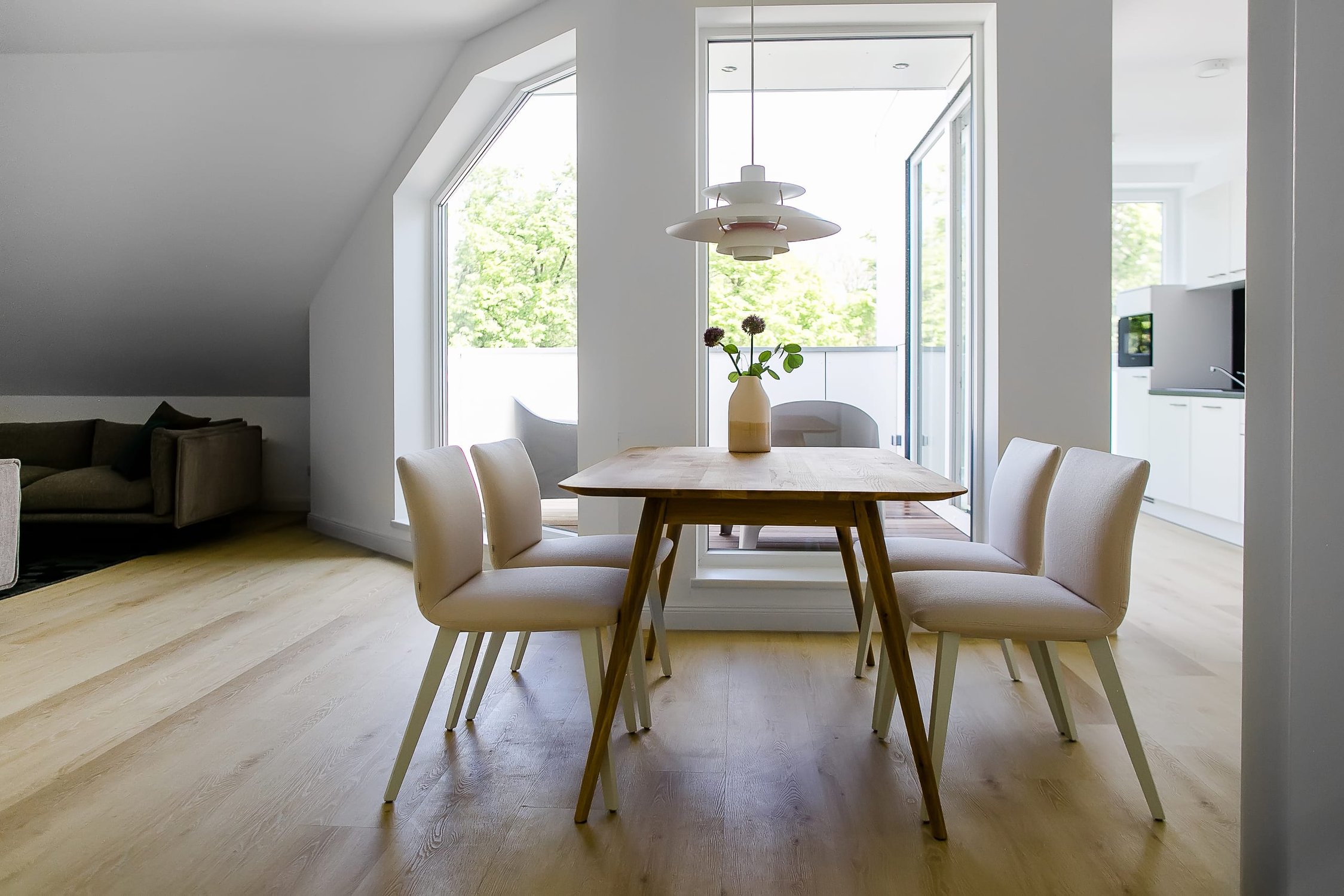 Wohn- und Essbereich mit Holzboden, weißem Esstisch, vier hellen Stühlen und Fensterfront