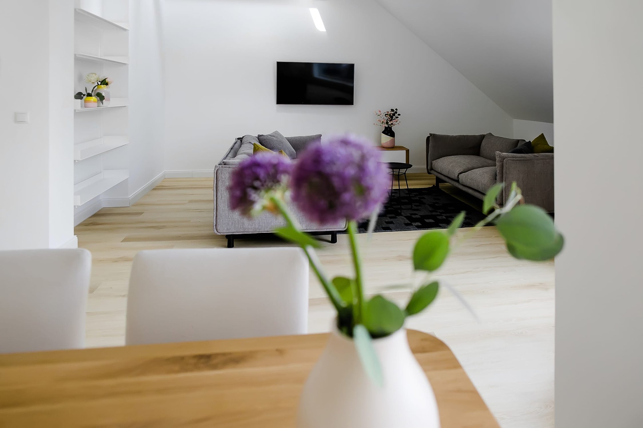 Helles Wohnzimmer mit lila Blumen auf Holztisch, Couch, und Wandregal