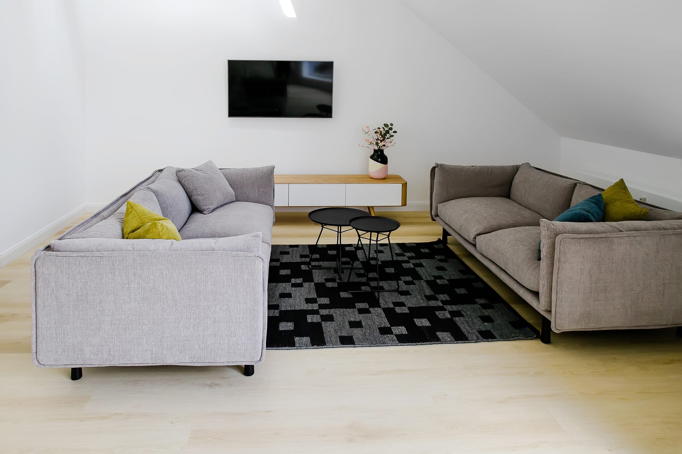 Dachwohnung-Wohnzimmer mit zwei grauen Sofas, Fernseher und dunklem Musterteppich auf hellem Holzboden