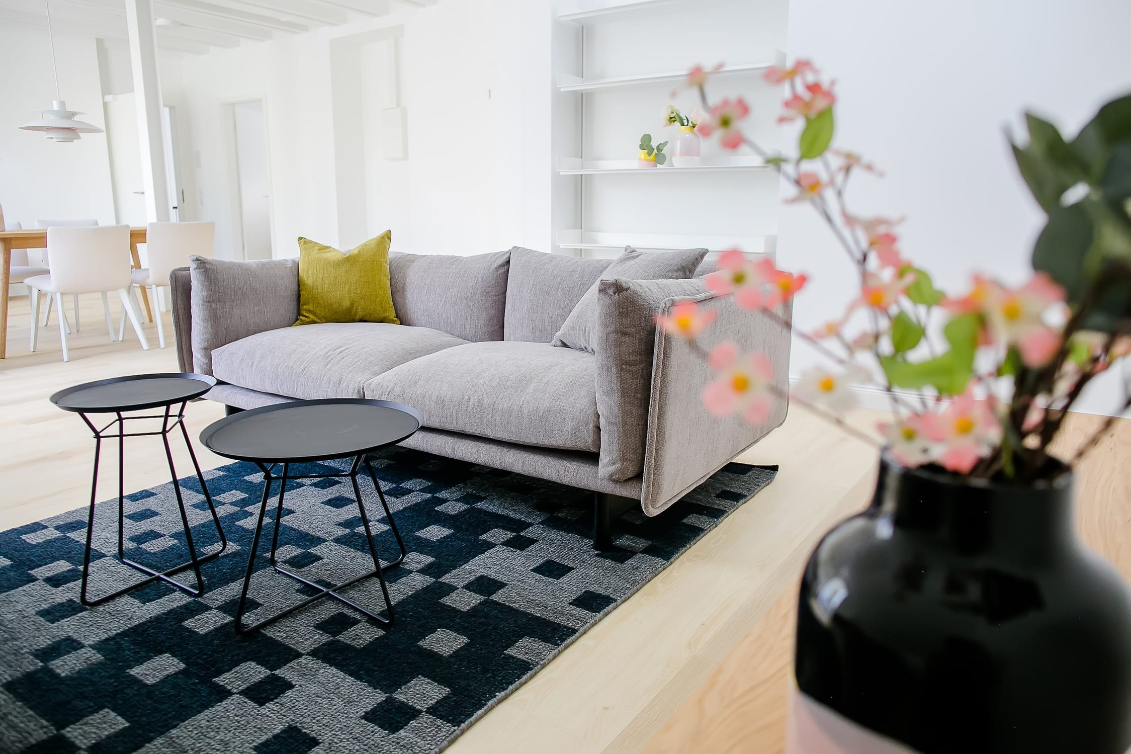 Helles Wohnzimmer mit grauem Sofa, zwei schwarzen Beistelltischen und blauem Teppich
