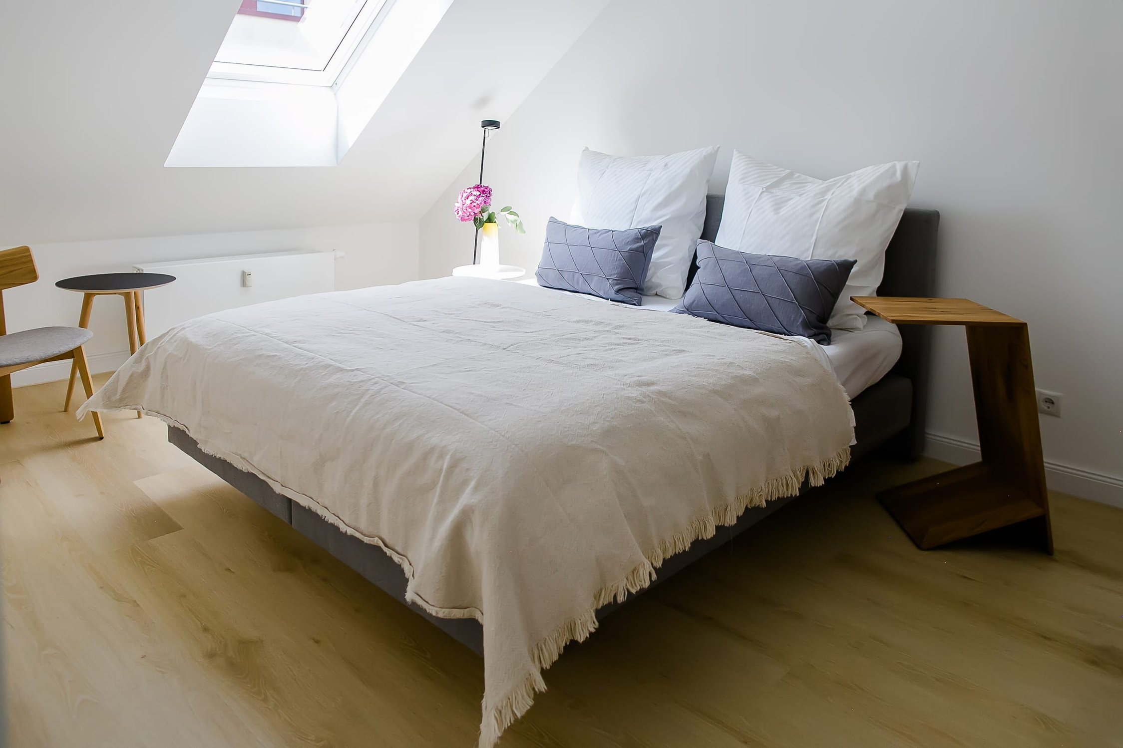 Helles Schlafzimmer mit Dachschräge, großem Bett, Holzboden und floraler Dekoration