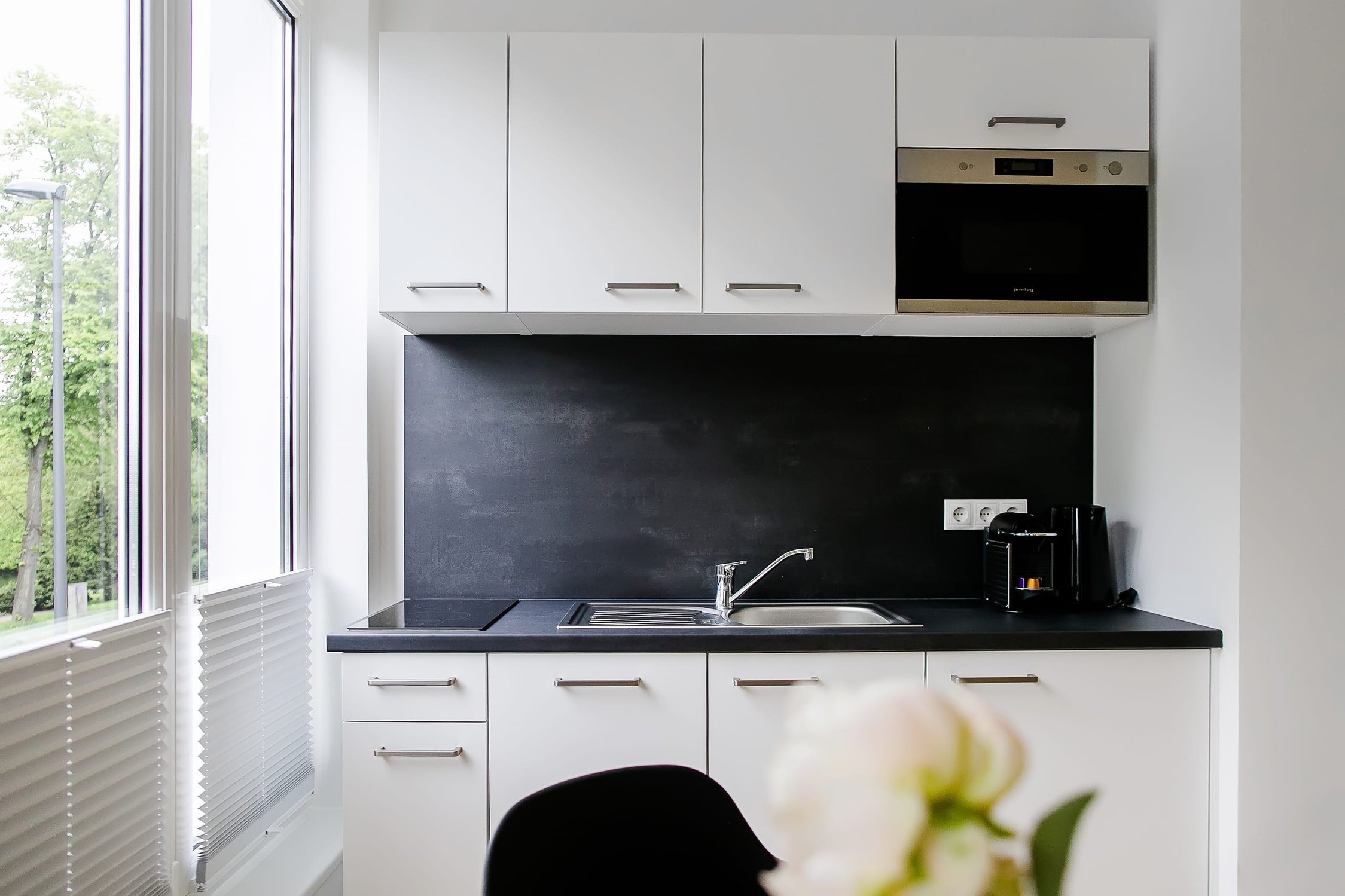 Moderne Küche mit weißen Schränken, dunkler Arbeitsplatte und großem Fenster