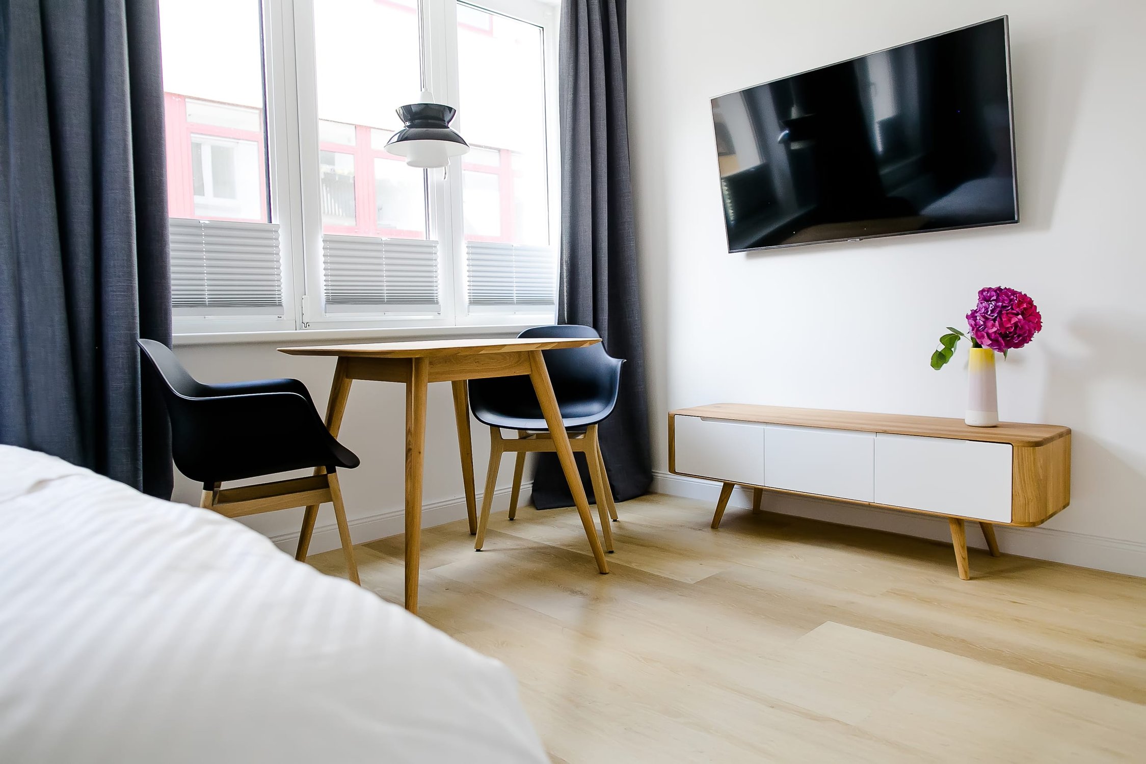 Zimmer mit Holztisch, schwarzen Stühlen, dunklen Vorhängen und Fernseher an weißer Wand