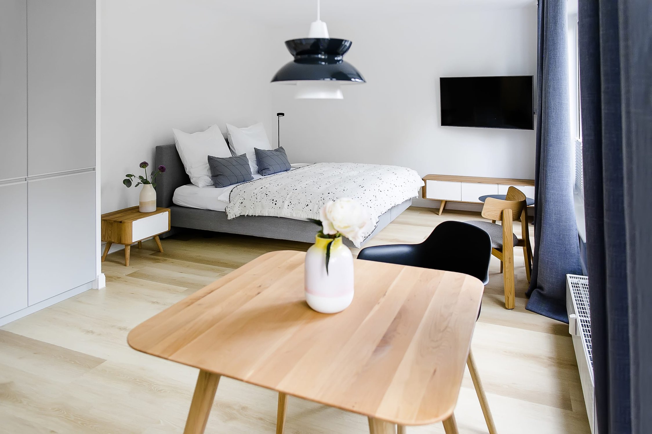 Modernes Schlafzimmer mit Bett, Holz-Esstisch und dunklen Vorhängen