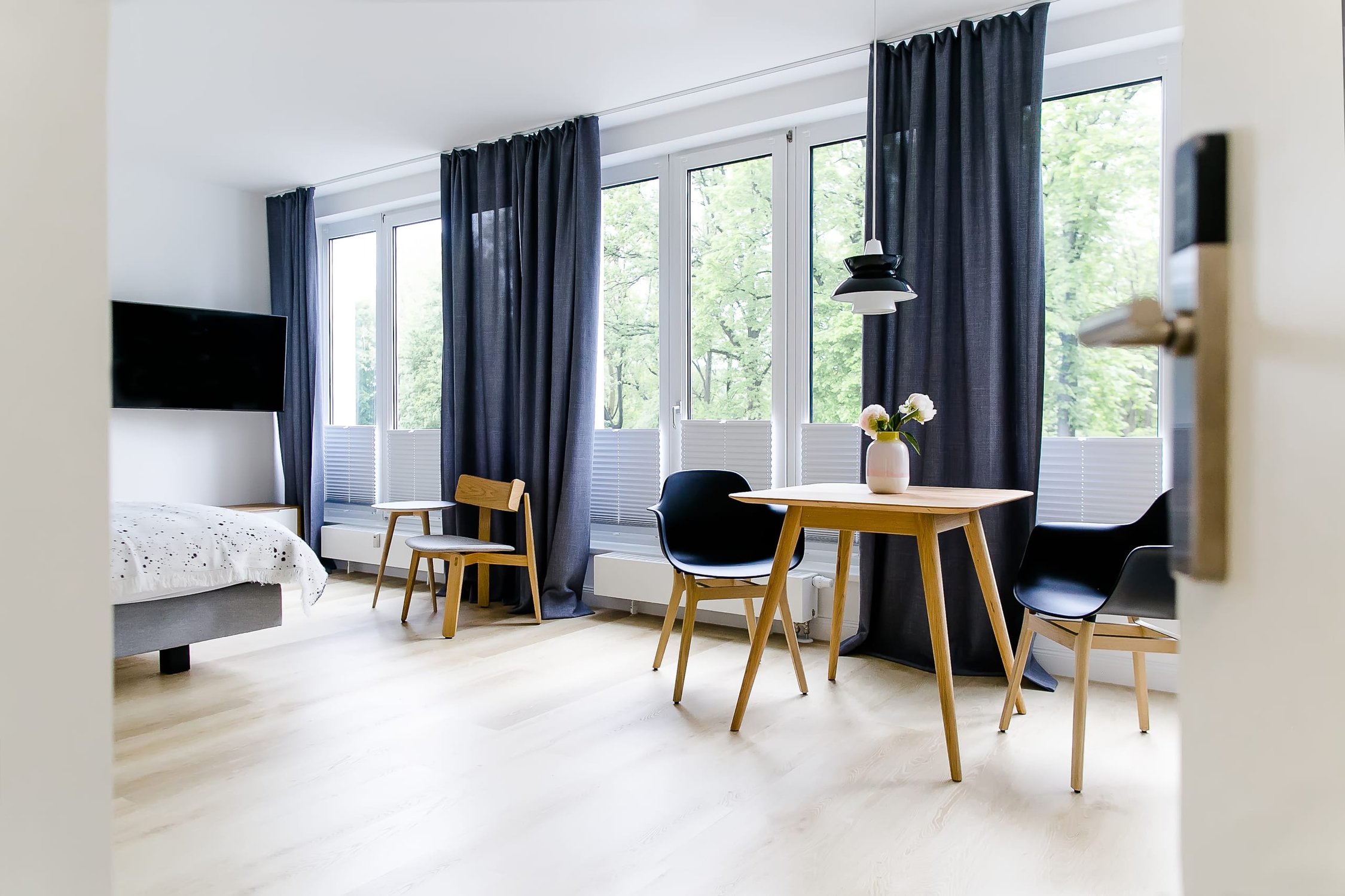 Helles Hotelzimmer mit hellbraunem Holzboden, großem Fenster und dunkelblauen Vorhängen