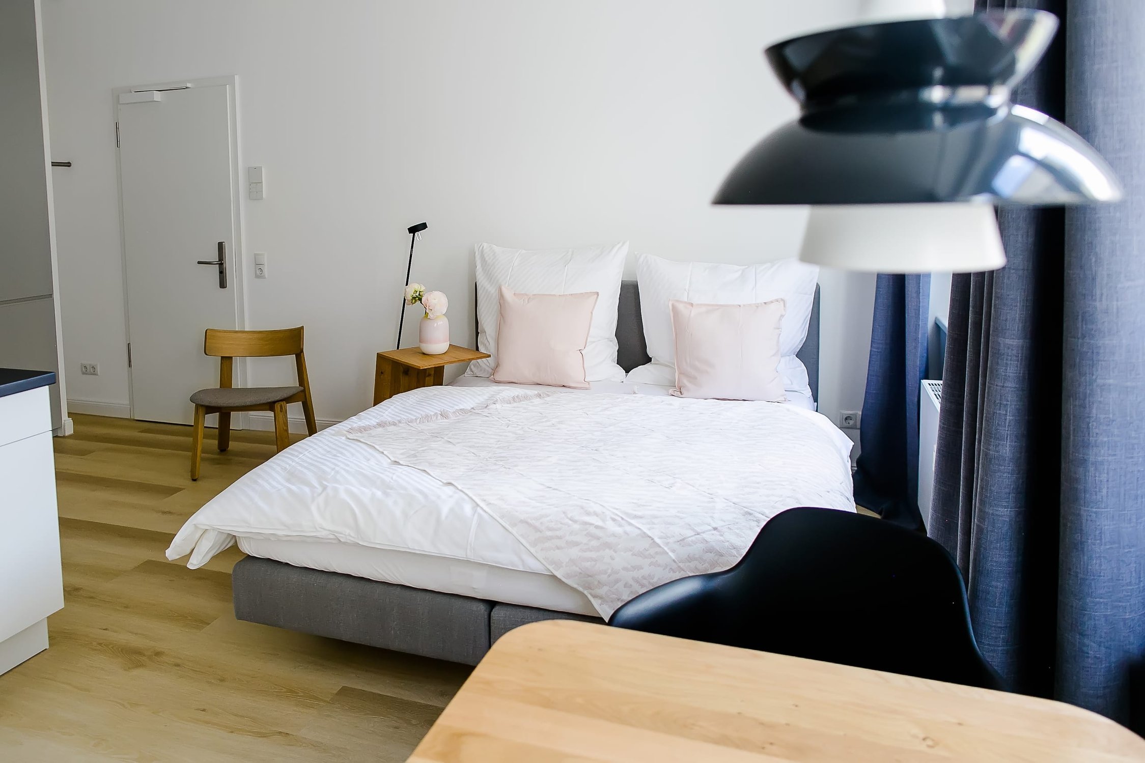Schlafzimmer mit weißem Bett, Holzmöbeln und dunkelblauen Vorhängen, moderne Lampe