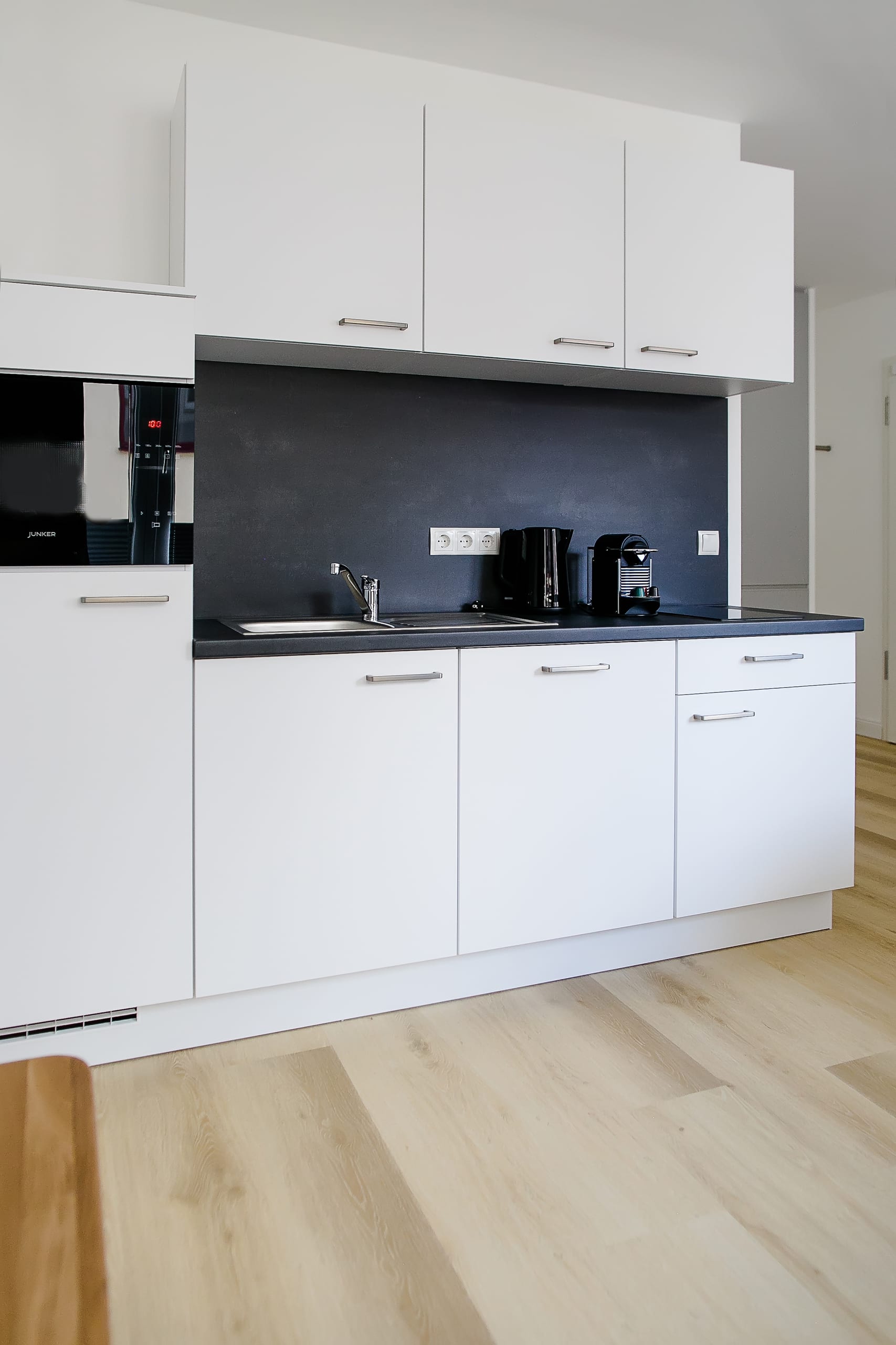 Moderne weiße Küchenzeile mit dunkler Arbeitsplatte, Spüle und hellbraunem Holzboden