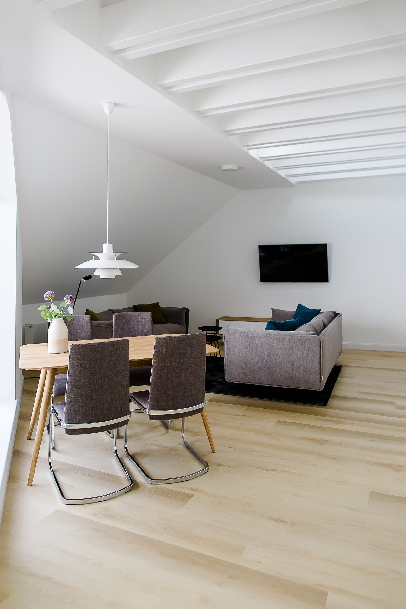 Heller Wohn- und Essbereich mit weißer Lampe, Holztisch, grauen Stühlen und Sofa