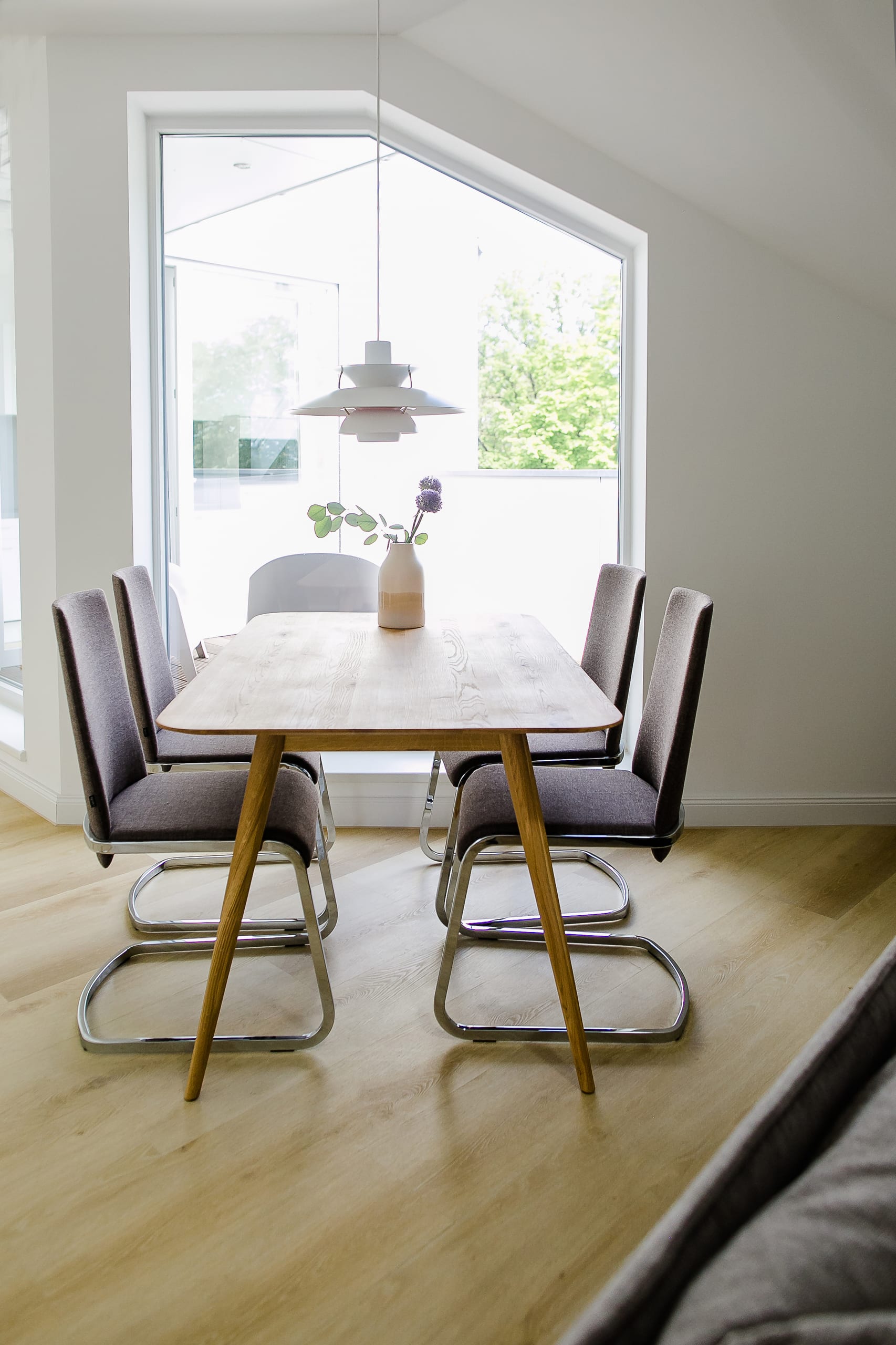 Esszimmer mit hellem Holztisch, dunkelgrauen Stühlen, Pendelleuchte, großem Fenster