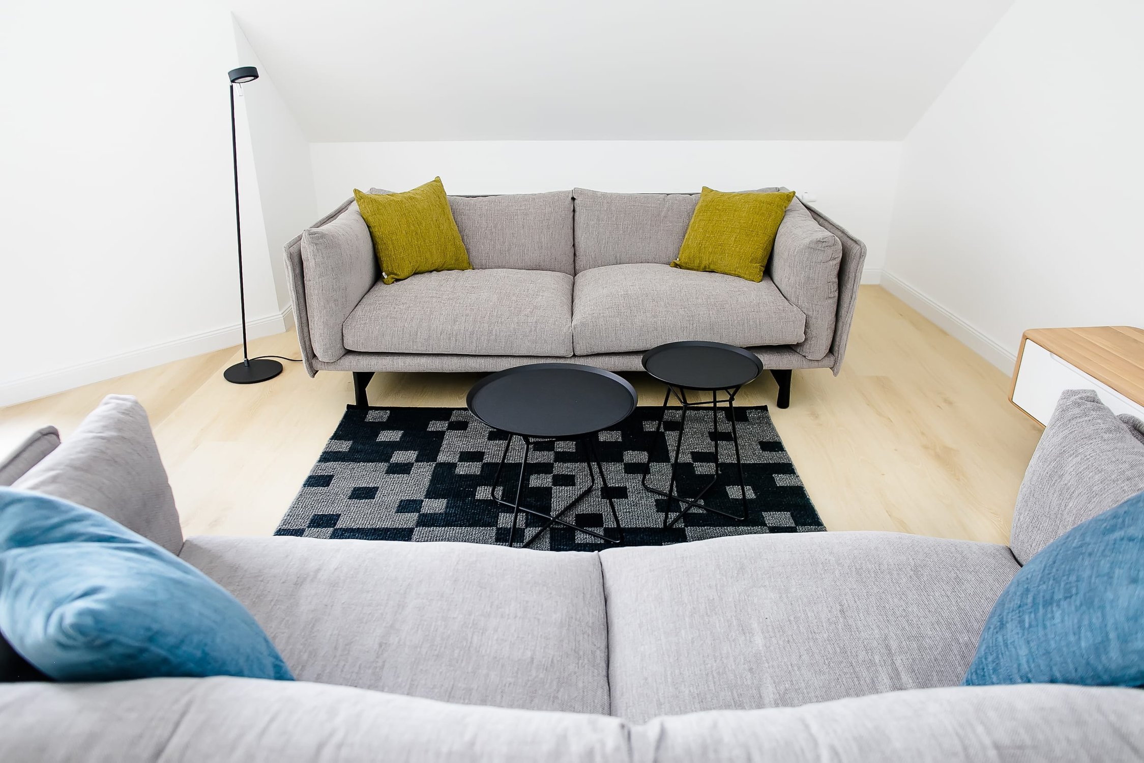 Modernes Wohnzimmer mit zwei grauen Sofas, gemusterter Teppich, zwei schwarzen Beistelltischen