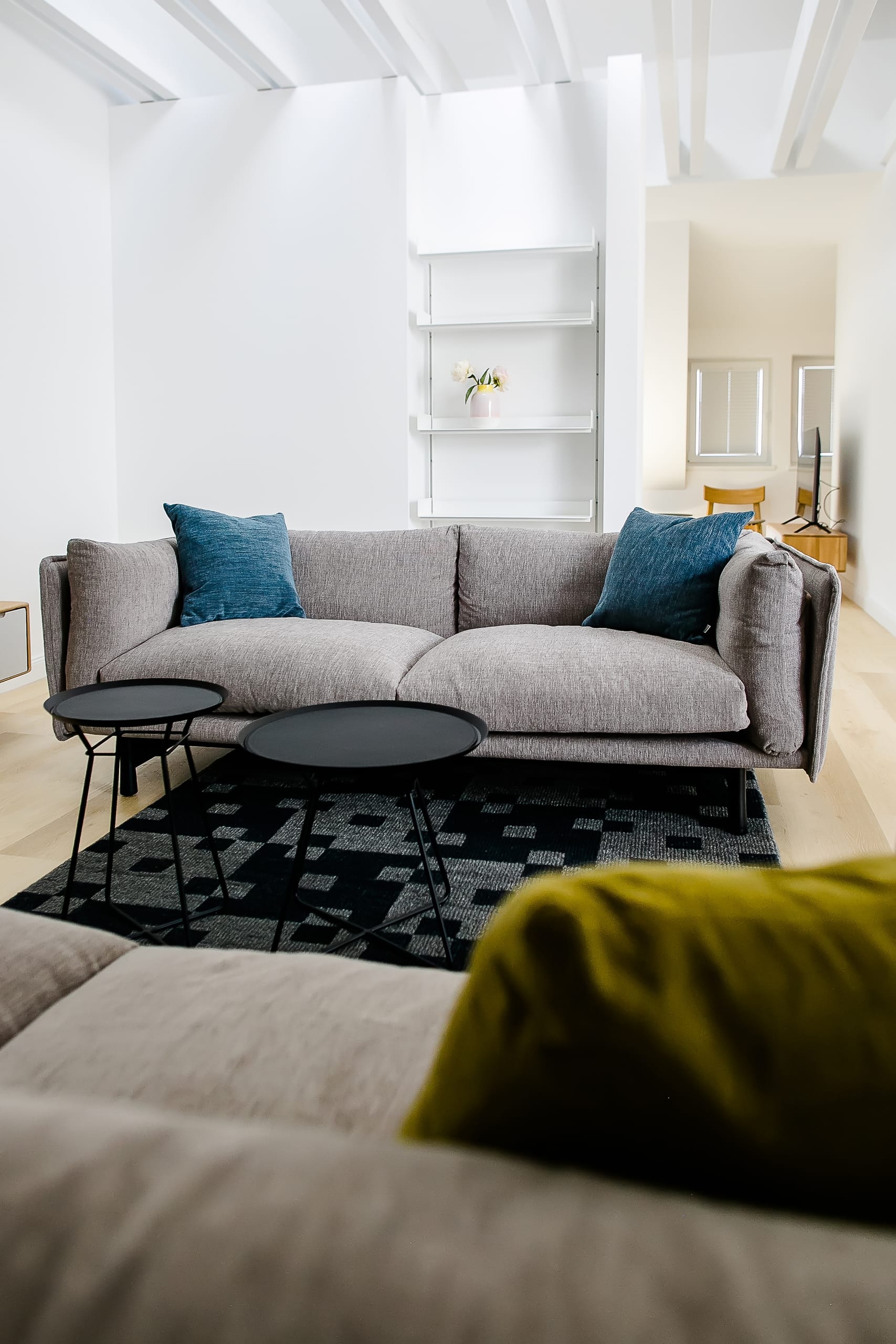 Modernes Wohnzimmer mit grauem Sofa, blauen Kissen, schwarzen Couchtischen und hellem Holzboden