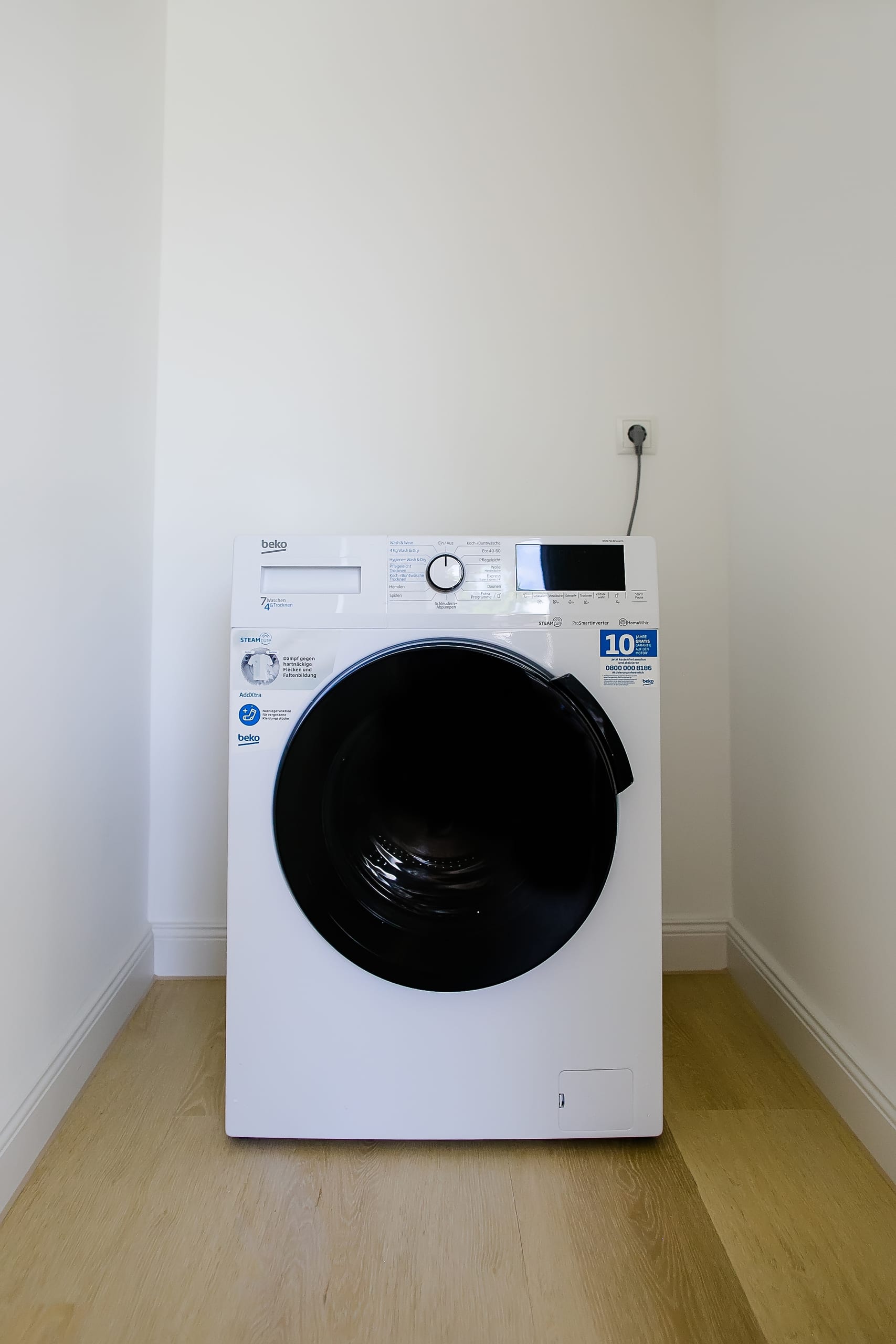 Weiße Waschmaschine mit dunkler Fronttür in hellem Raum mit Holzfußboden