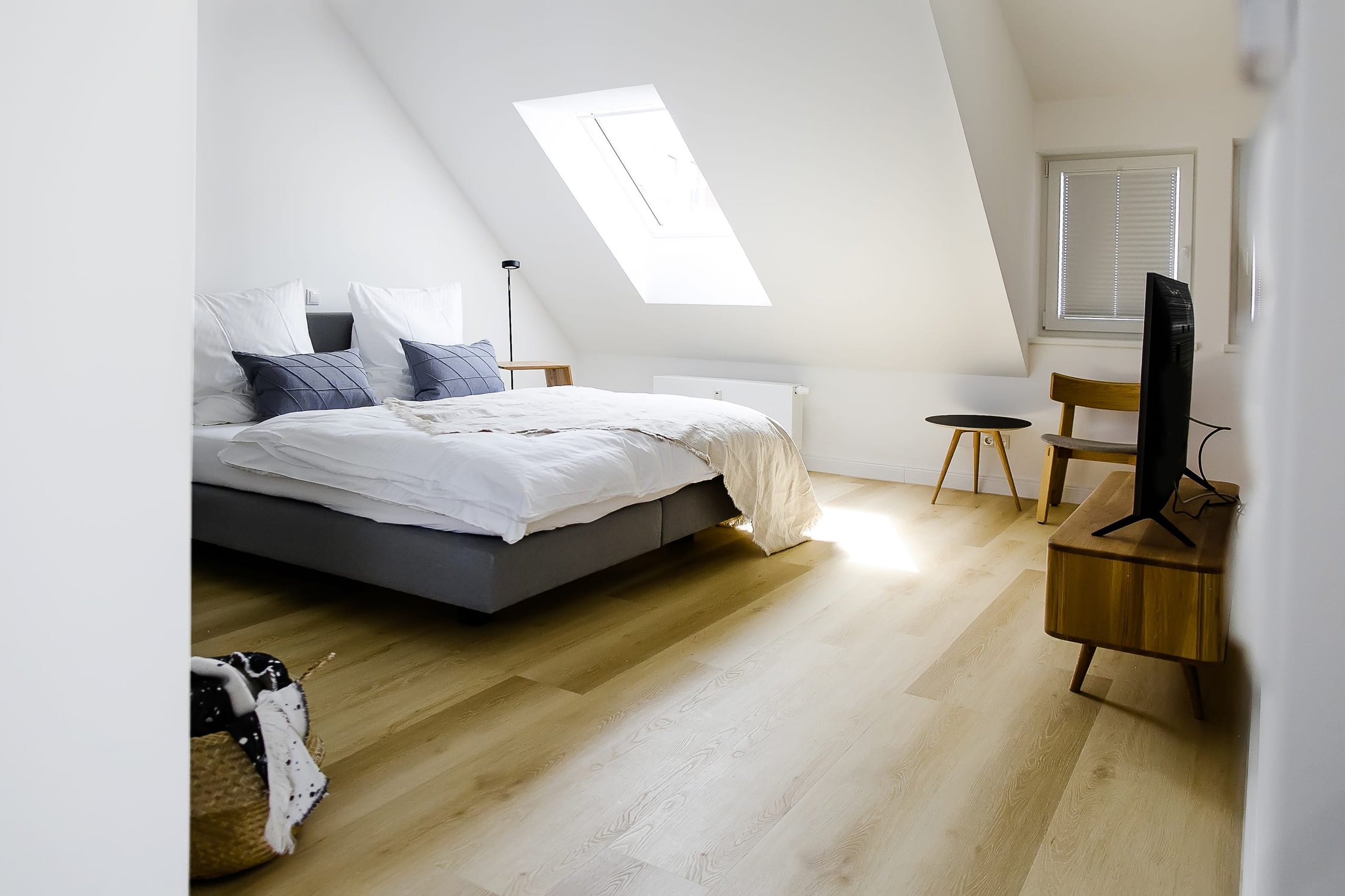 Dachgeschoss-Schlafzimmer mit großem Bett, heller Holzoptikboden, TV und Dachfenster