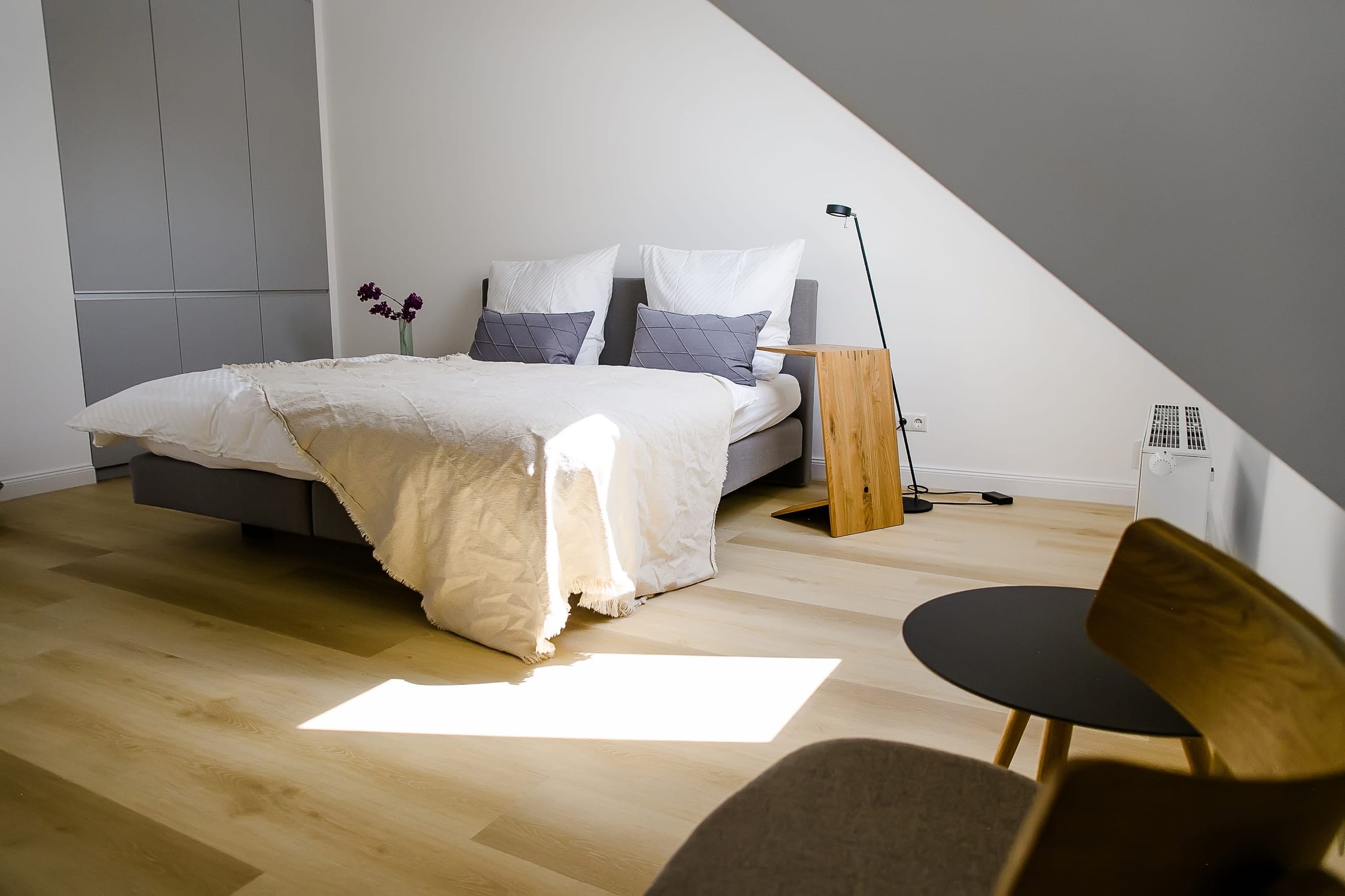 Modernes Schlafzimmer mit Doppelbett, hellem Holzboden und grauen Möbeln, Dachschräge