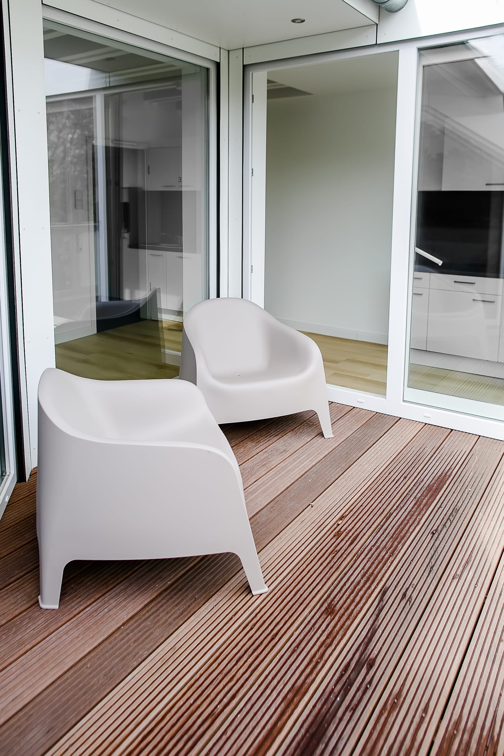 Balbkon mit zwei hellgrauen Stühlen und Holzfliesen, Glasfassade im Hintergrund