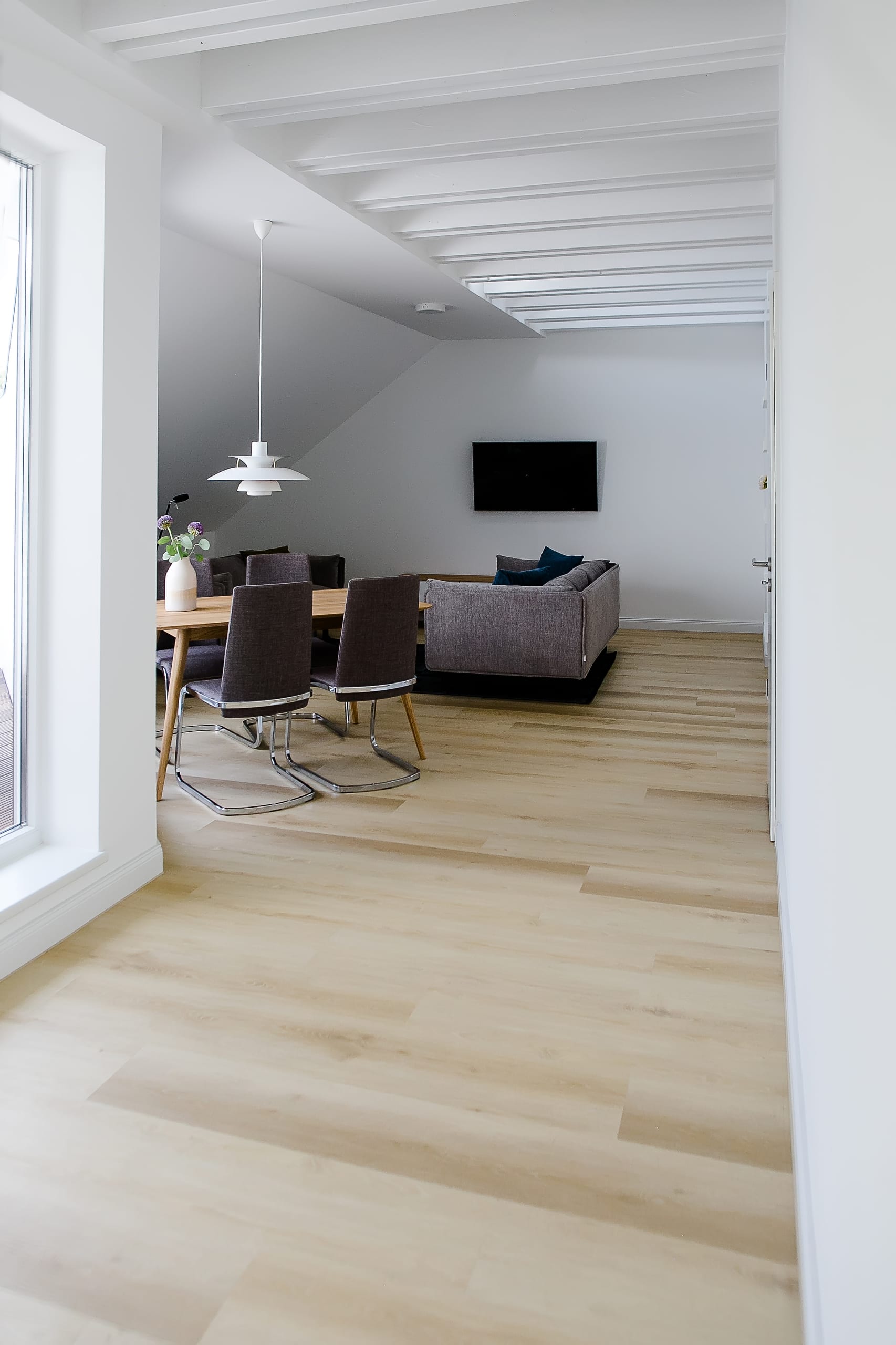 Helles Wohnzimmer mit Holzboden, Esstisch, grauen Stühlen und Sofa