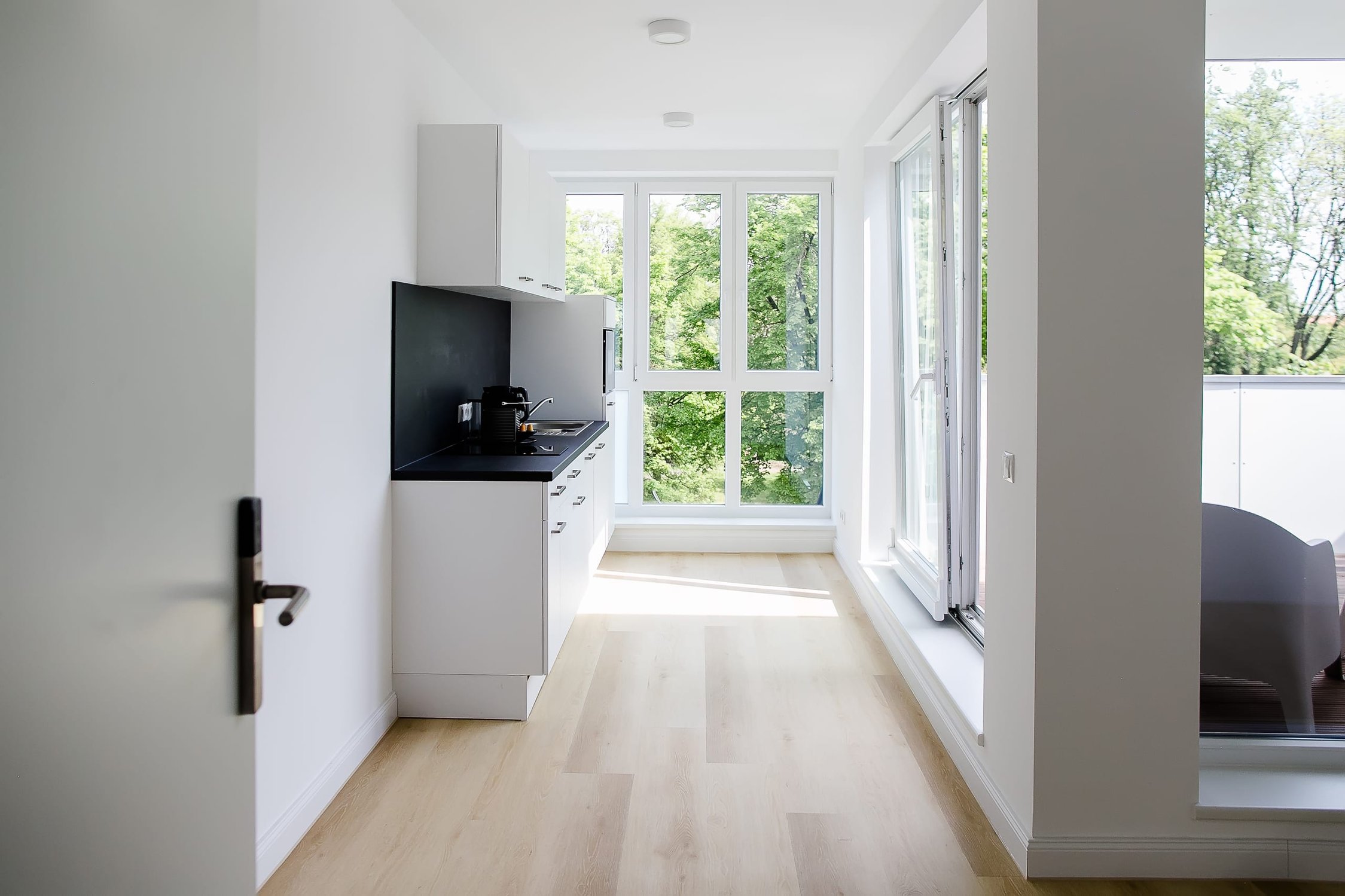 Lange, helle Küchenzeile mit weißen Schränken, dunkler Arbeitsplatte, Fensterfront