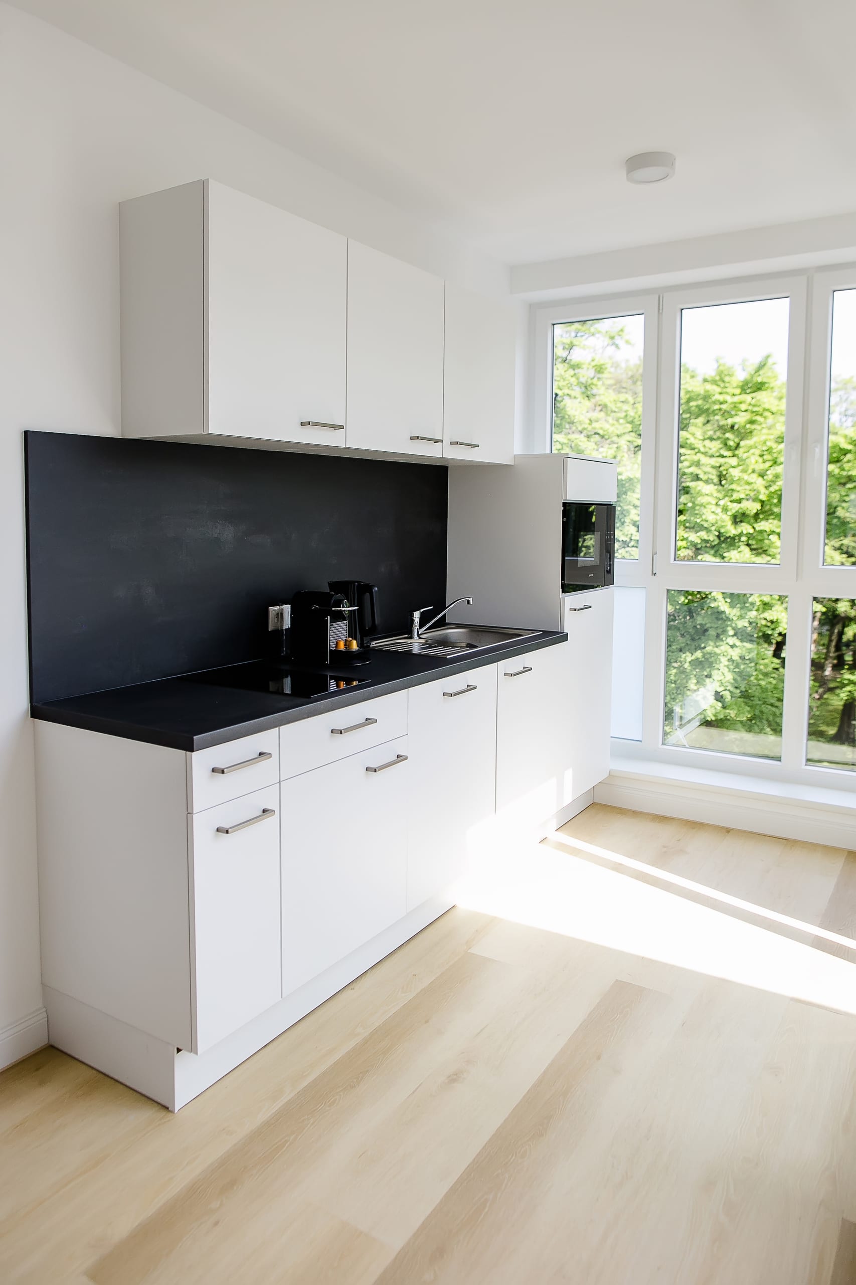 Helle Küche mit weißen Schränken, dunkler Arbeitsplatte, großem Fenster, hellbraunem Holzboden