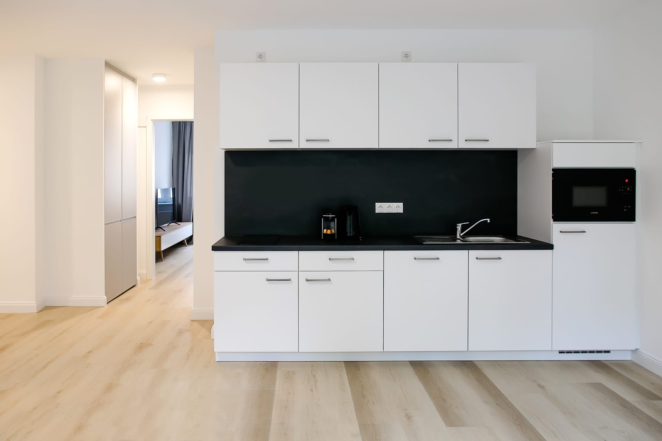 Moderne Küchenzeile in Weiß mit schwarzer Arbeitsplatte, Spüle und Mikrowelle, Holzfußboden