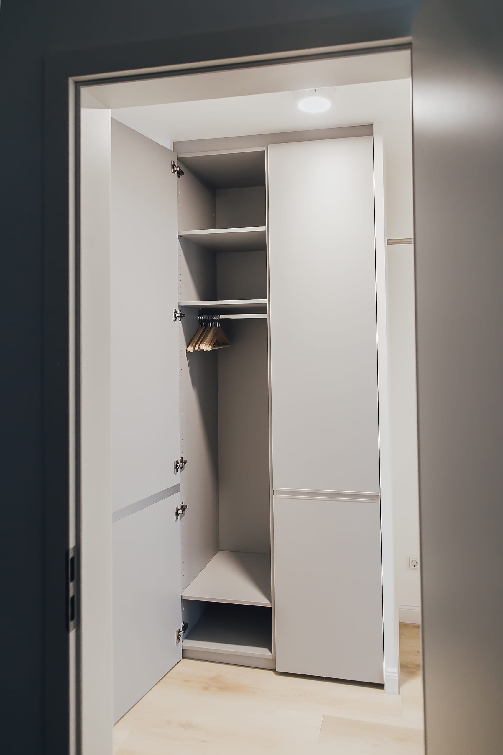 Offener grauer Kleiderschrank mit zwei Türen, Regalen, Kleiderstange und Holzkleiderbügeln