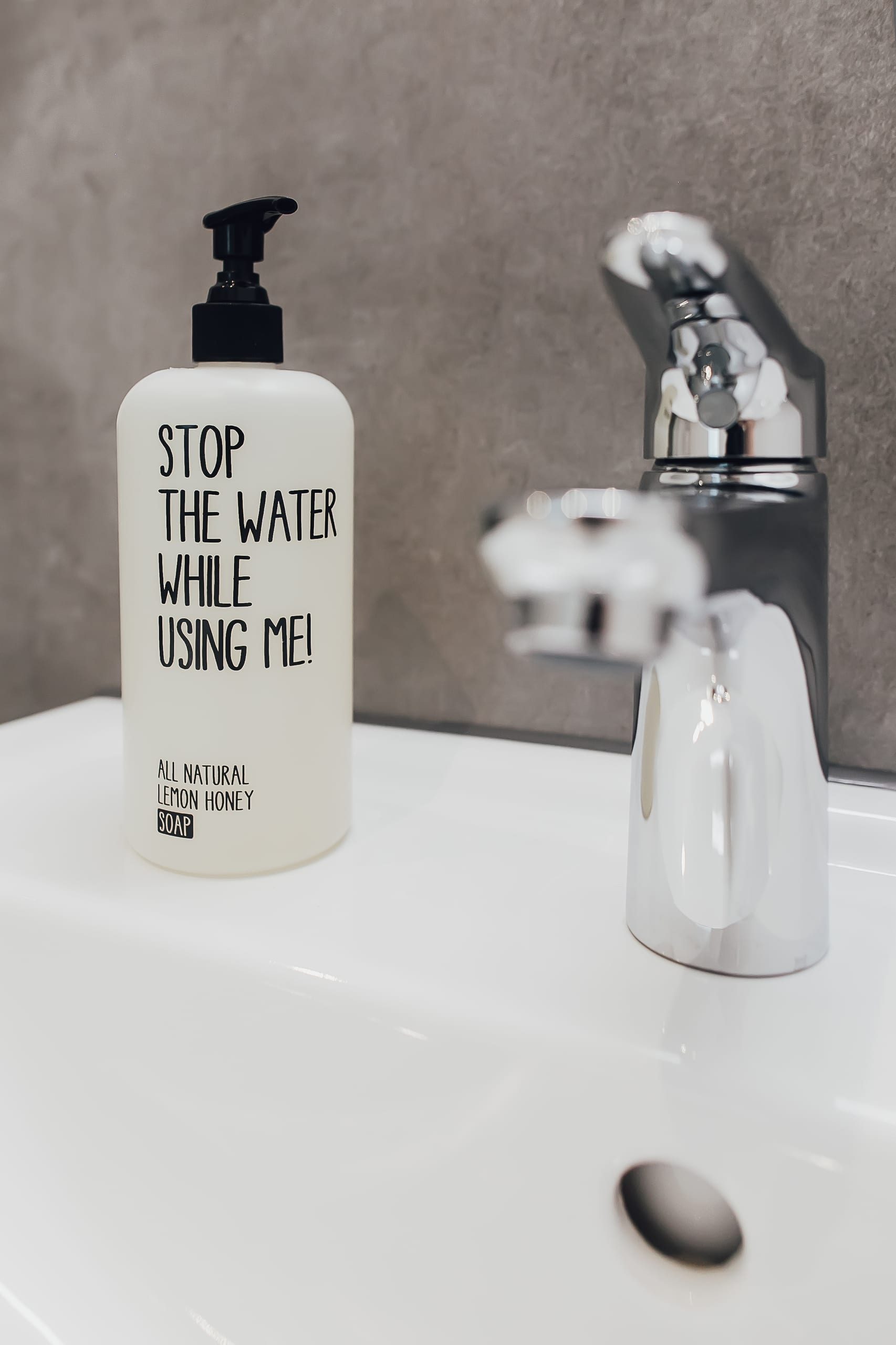 Seifenspender mit Aufschrift "Stop the water...", Wasserhahn auf weißem Waschbecken