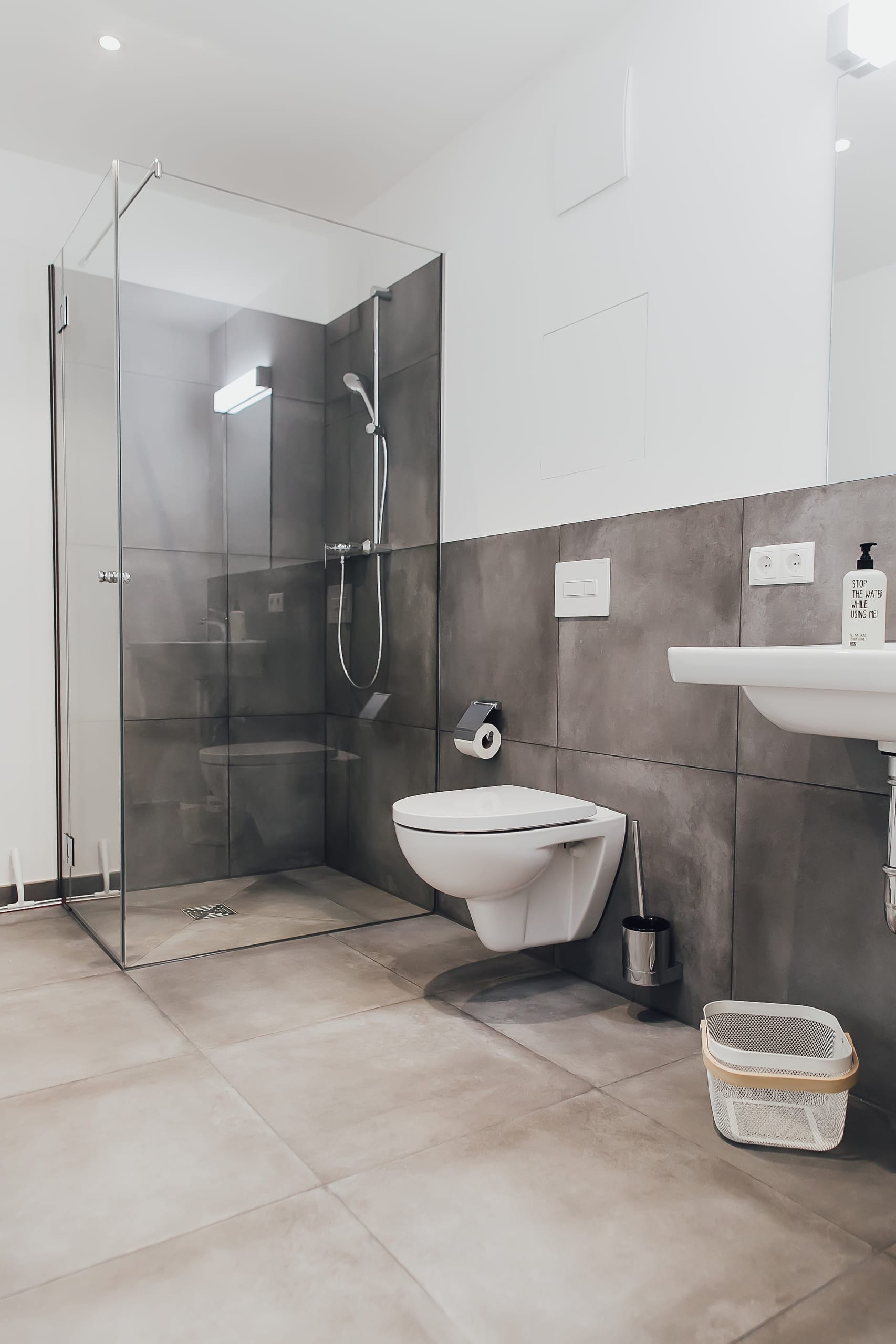 Modernes Badezimmer mit grauen Fliesen, offener Glasdusche und weißem WC