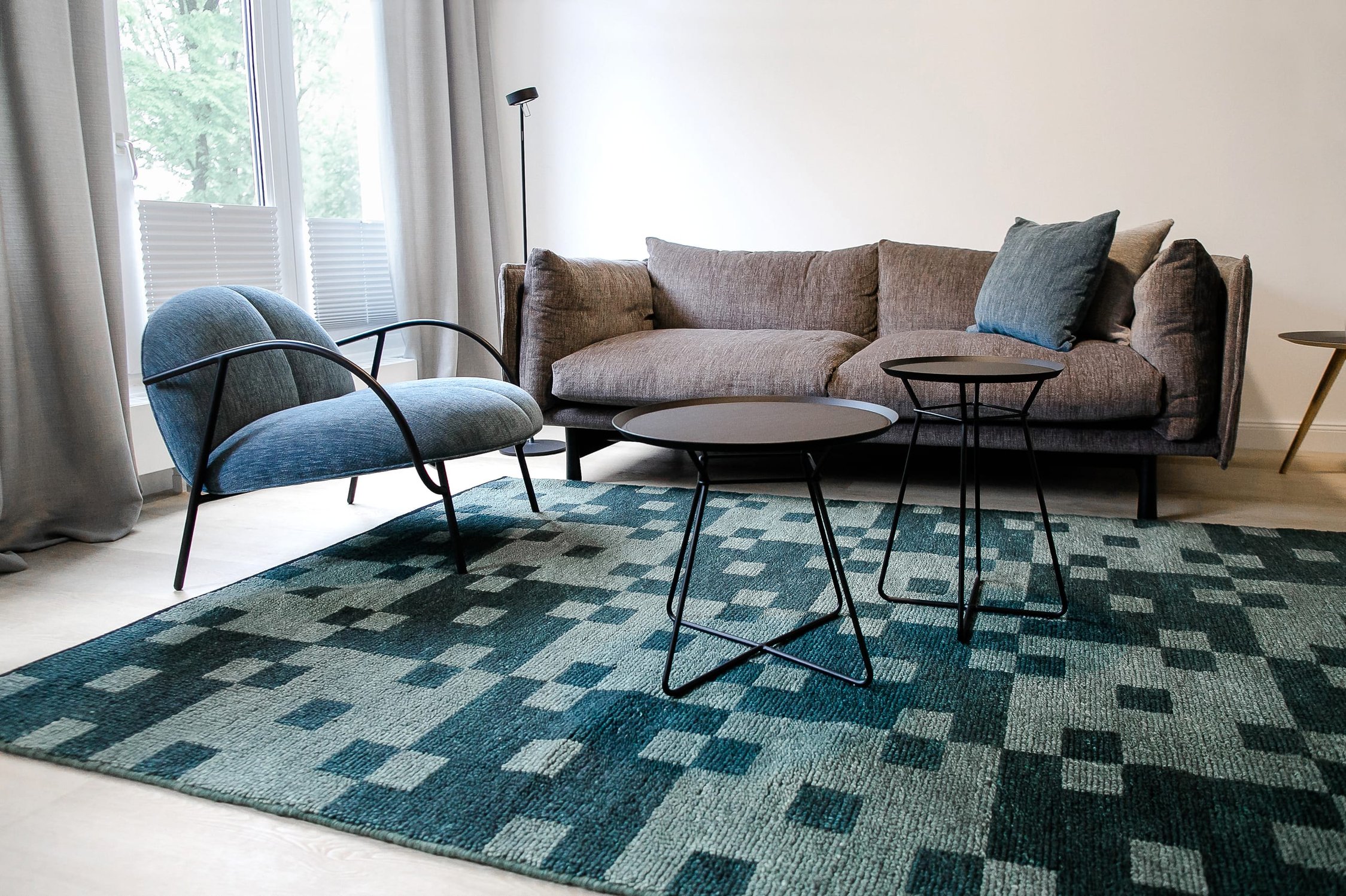 Modernes Wohnzimmer mit braunem Sofa, blauem Sessel, zwei schwarzen Beistelltischen und geometrischem Teppich