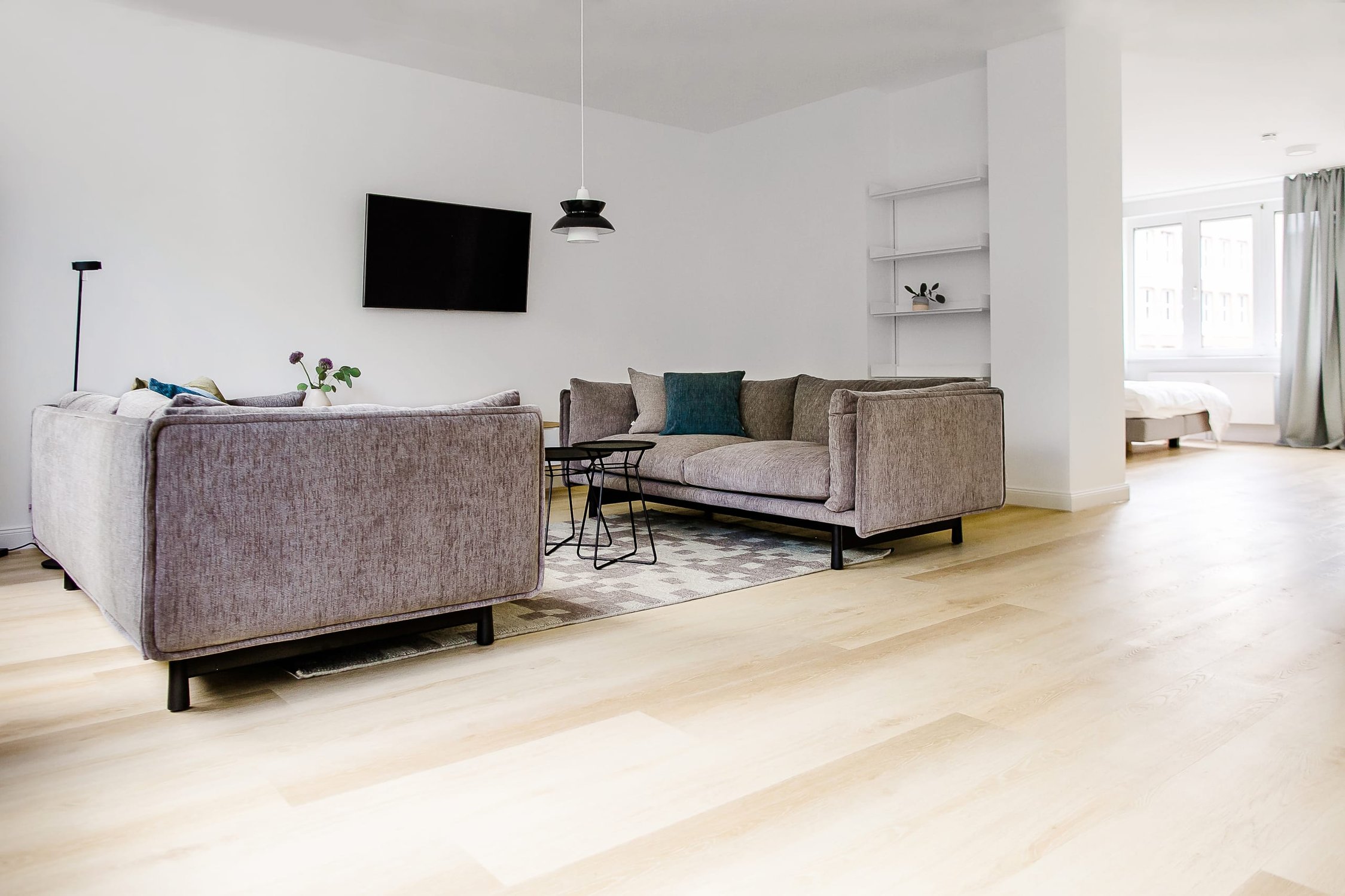Helles Wohnzimmer mit zwei grauen Sofas, Fernseher, Holzboden und Blick auf Schlafzimmer