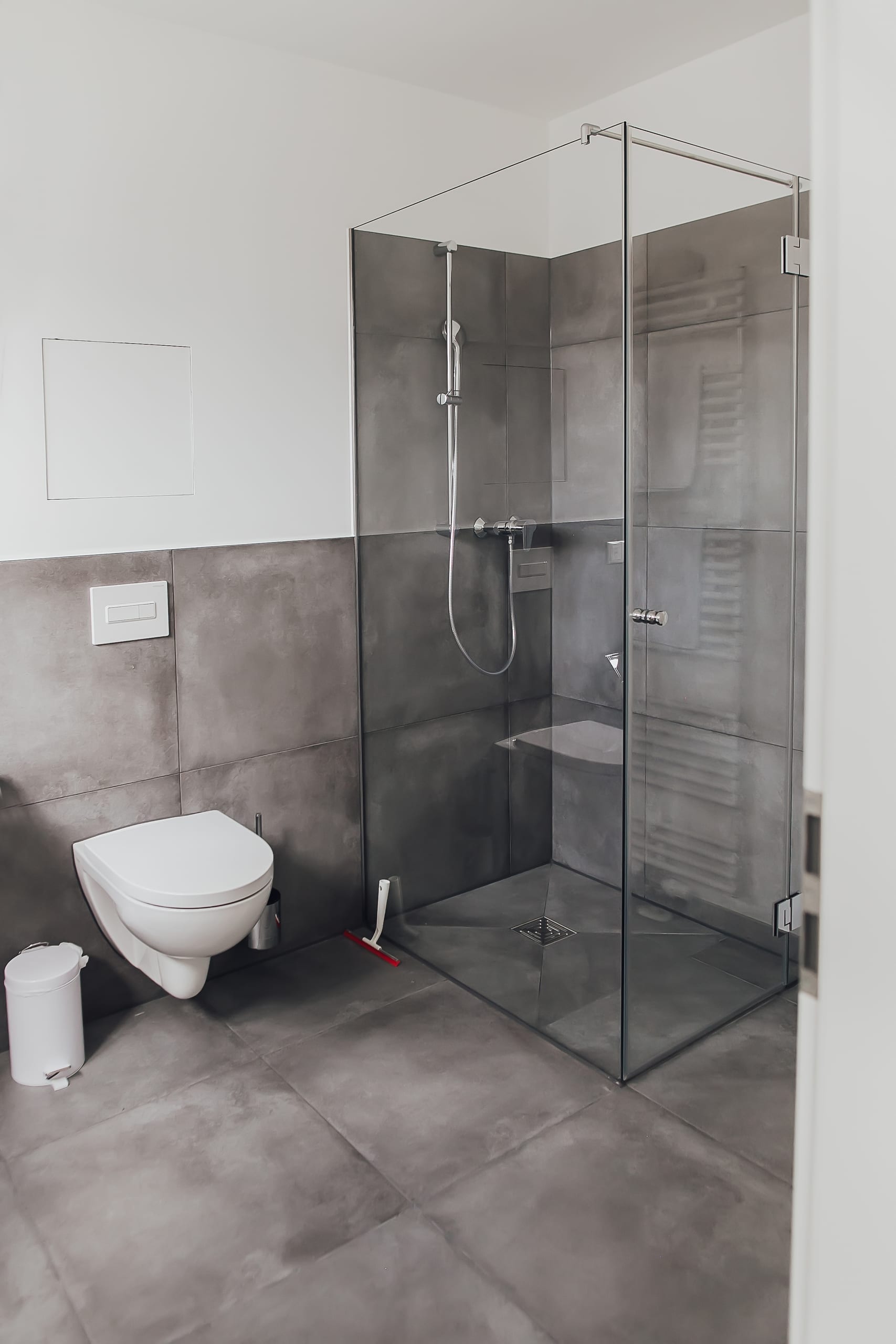 Modernes Badezimmer mit wandhängender Toilette, Duschkabine aus Glas und dunkelgrauen Fliesen