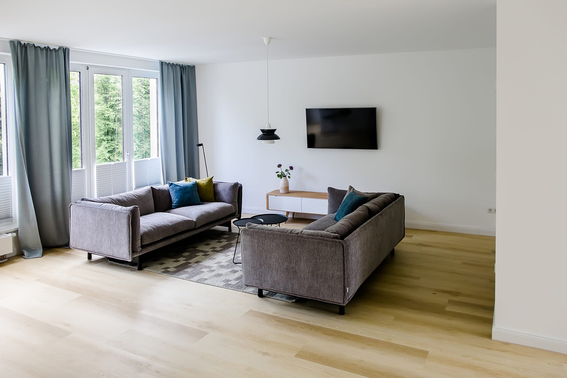 Wohnzimmer mit zwei grauen Sofas auf hellem Parkett, TV-Gerät an weißer Wand