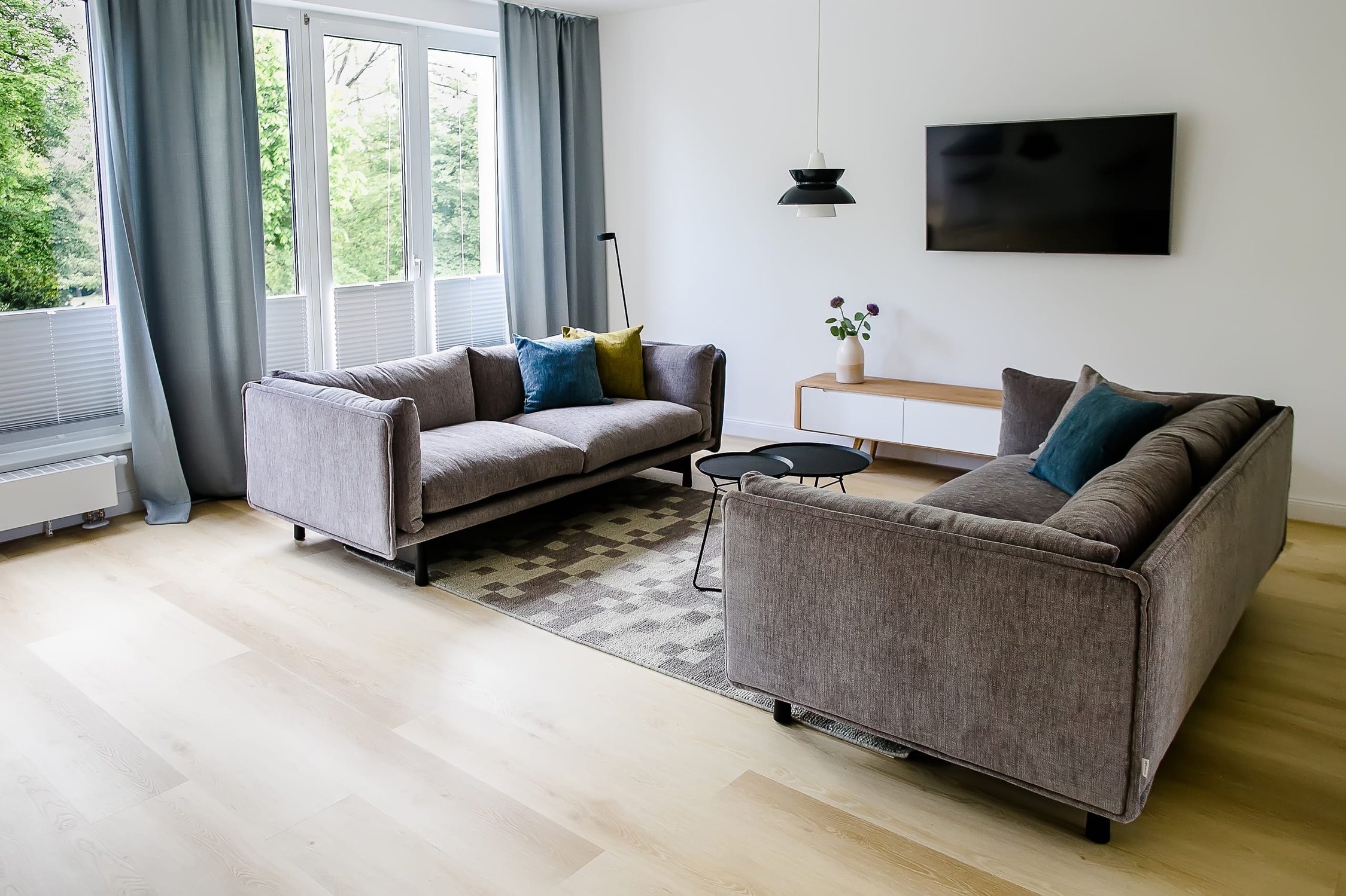 Helles Wohnzimmer mit zwei grauen Sofas, großem Fenster, Vorhängen und Holzboden