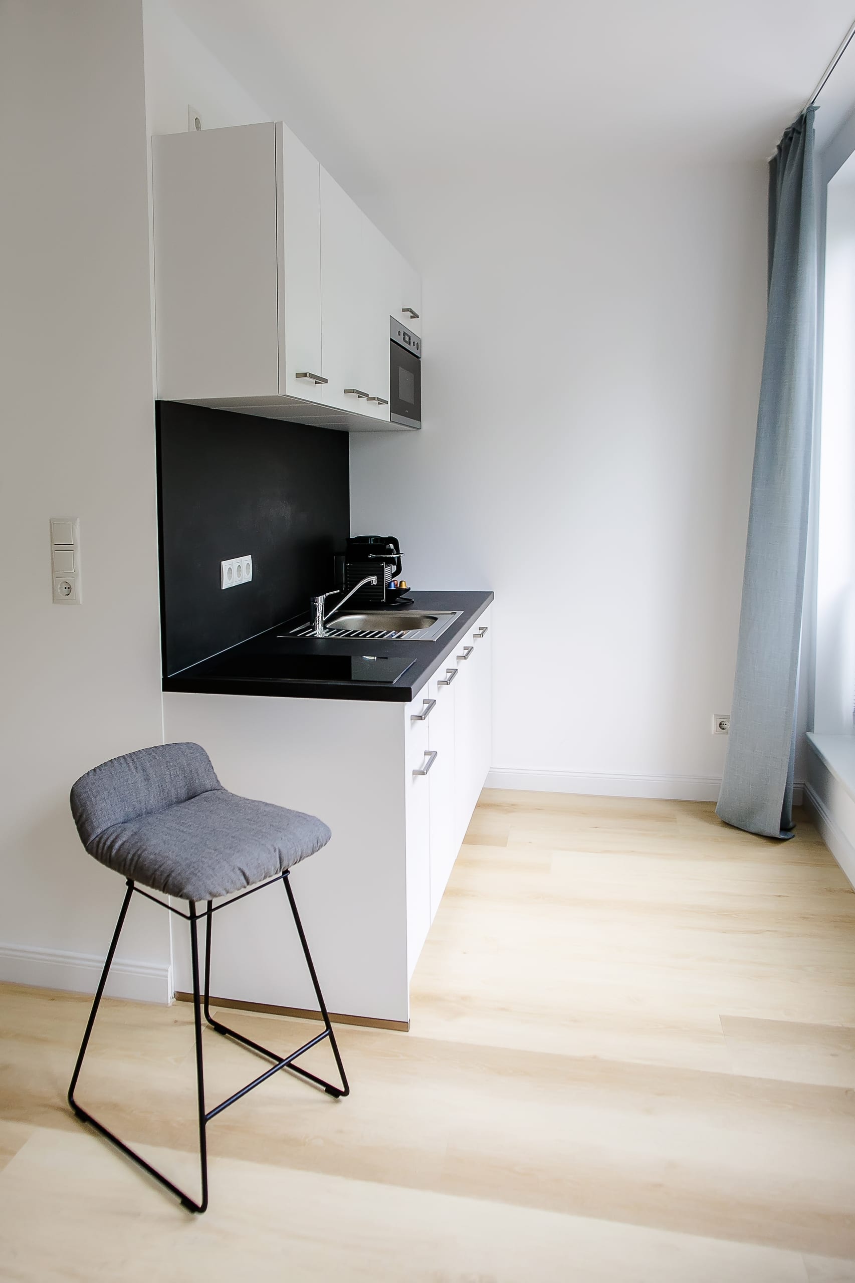 Kleine Küche mit weißer Küchenzeile, schwarzer Arbeitsplatte und einem Barhocker