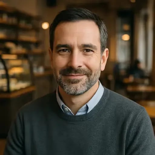 Mann mit Bart im Café, blaues Hemd und grauer Pullover, Blick in die Kamera