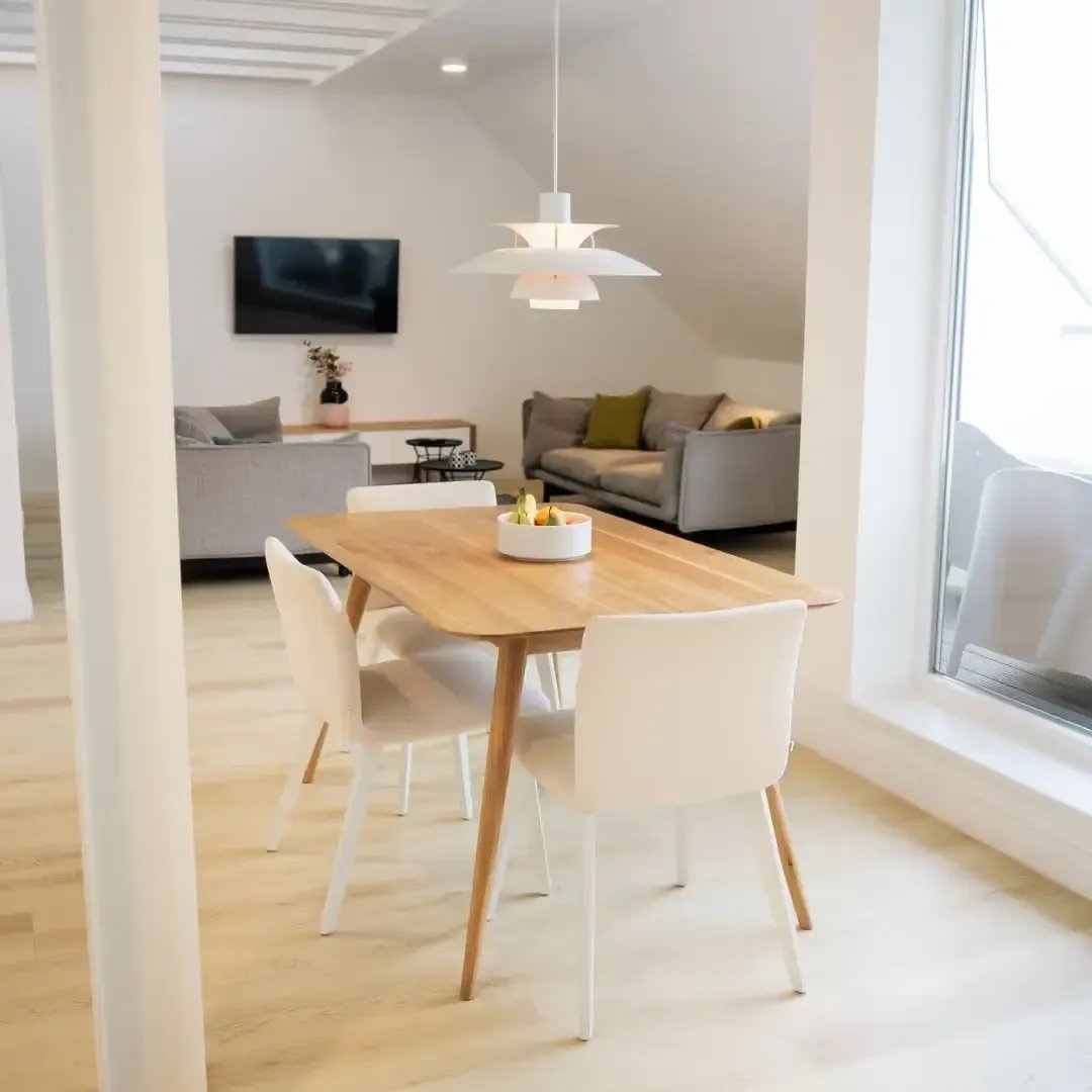 Offener heller Wohnraum mit Holztisch für vier Personen, Pendelleuchte, Sofas und TV