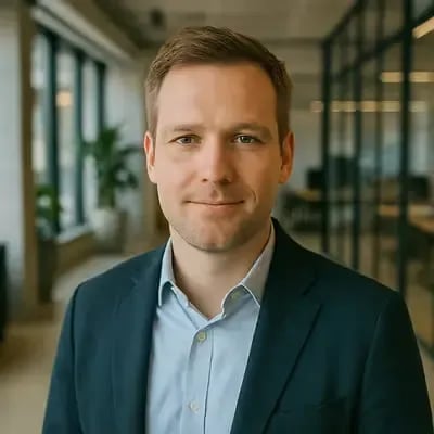 Person mit hellem Haar und Bartstoppeln in Anzug und Hemd, Bürohintergrund