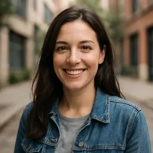 Lachende Person mit langen, braunen Haaren in Jeansjacke und grauem T-Shirt, vor Häuserfassaden