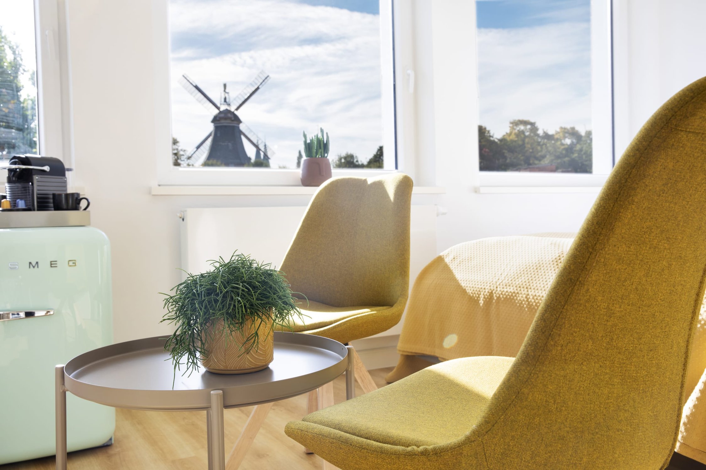Heller Wohnraum mit zwei gelben Stühlen, kleinem Tisch und Windmühle im Hintergrund